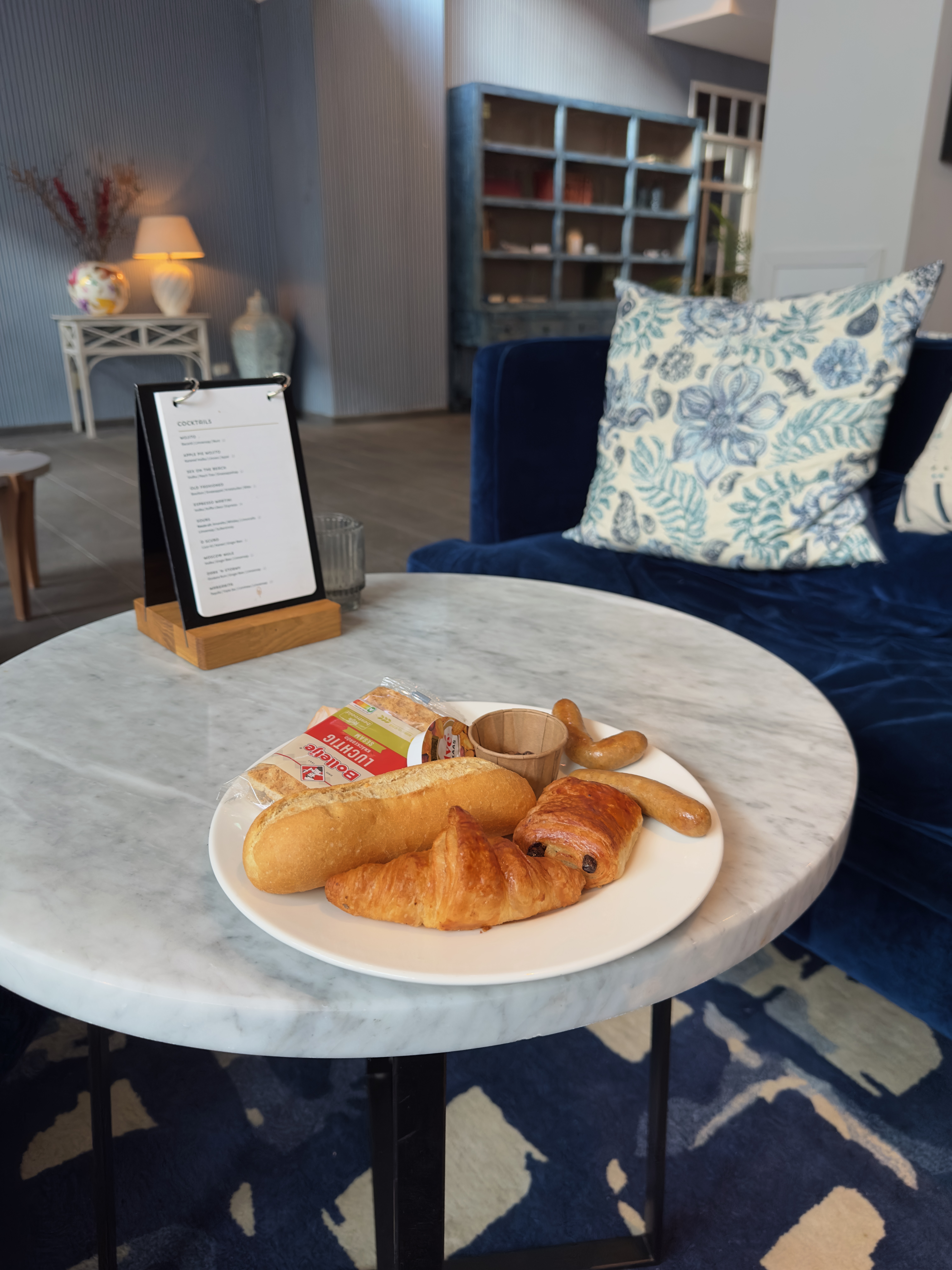 Grand Hotel Ter Duin review – breakfast selection with croissant, chocolate pastry, bread roll and sausages on a marble table in the elegant lounge area of the hotel.