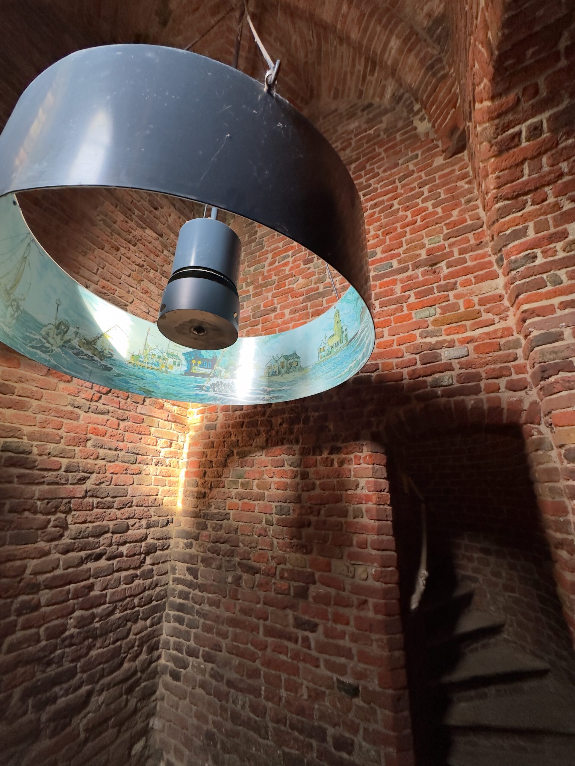 Plompe Toren Koudekerke interior spiral staircase and historic brick walls beneath suspended maritime illustration display