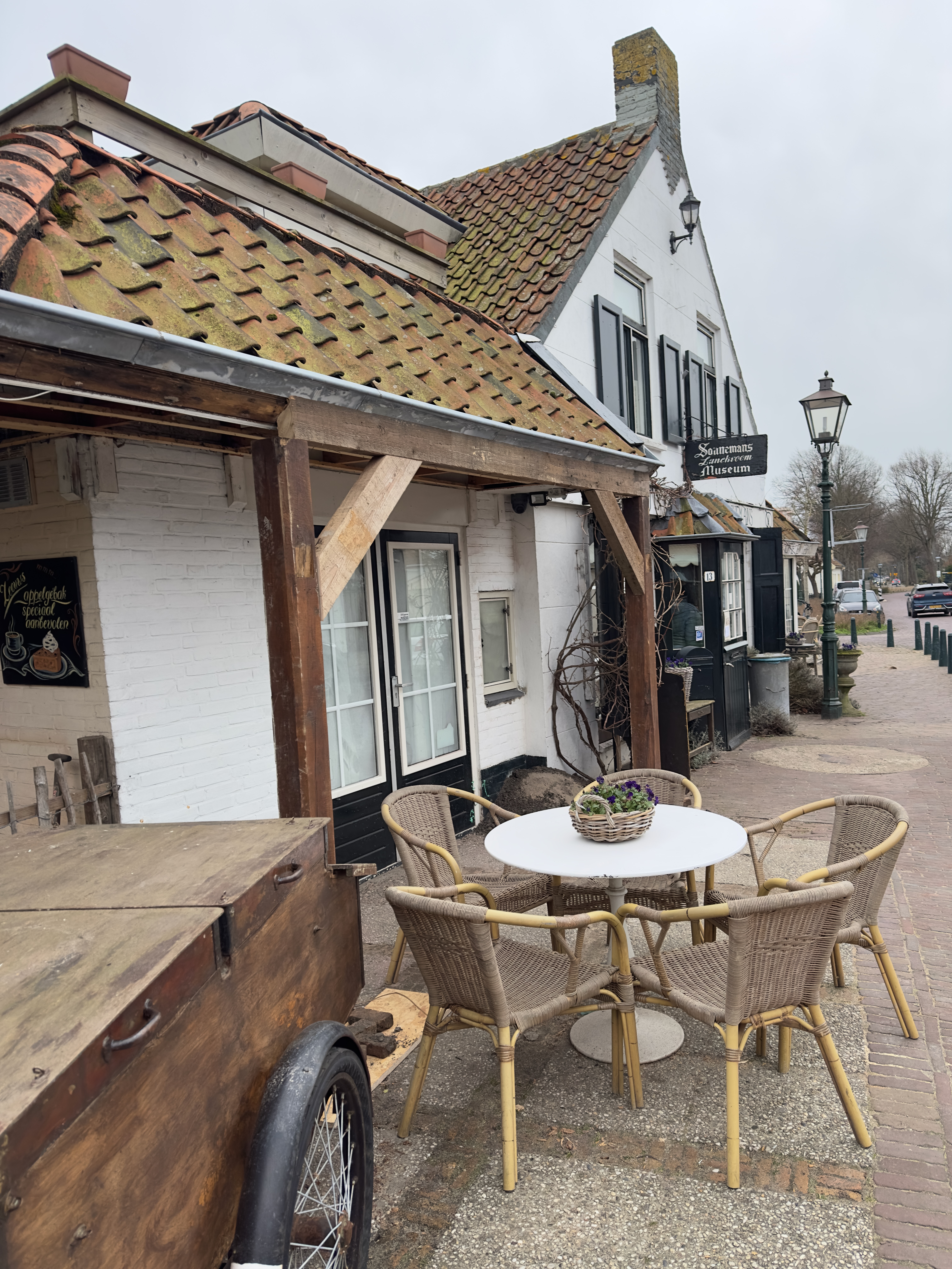 Bakkerij Sonnemans in Burgh Haamstede outdoor terrace with wicker chairs, round table, rustic white facade and moss covered roof tiles along quiet village street
