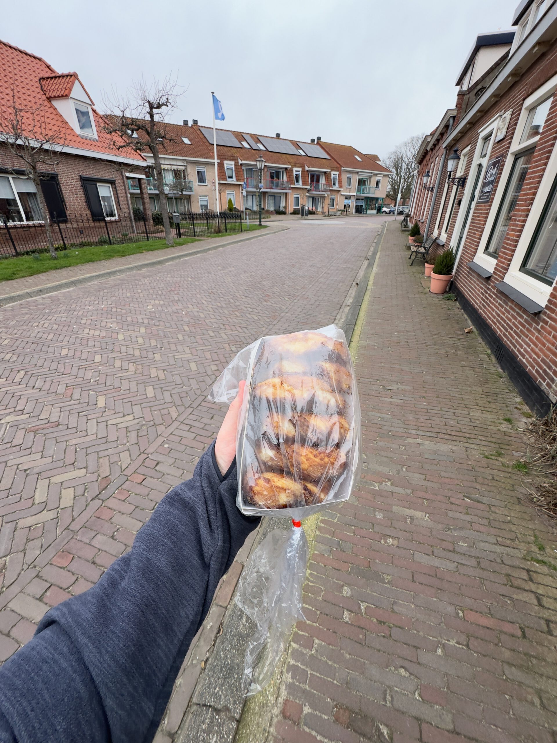 Bakkerij Sonnemans in Burgh Haamstede Zeeuwse bolussen takeaway held in hand on quiet village street with brick houses and Dutch flag