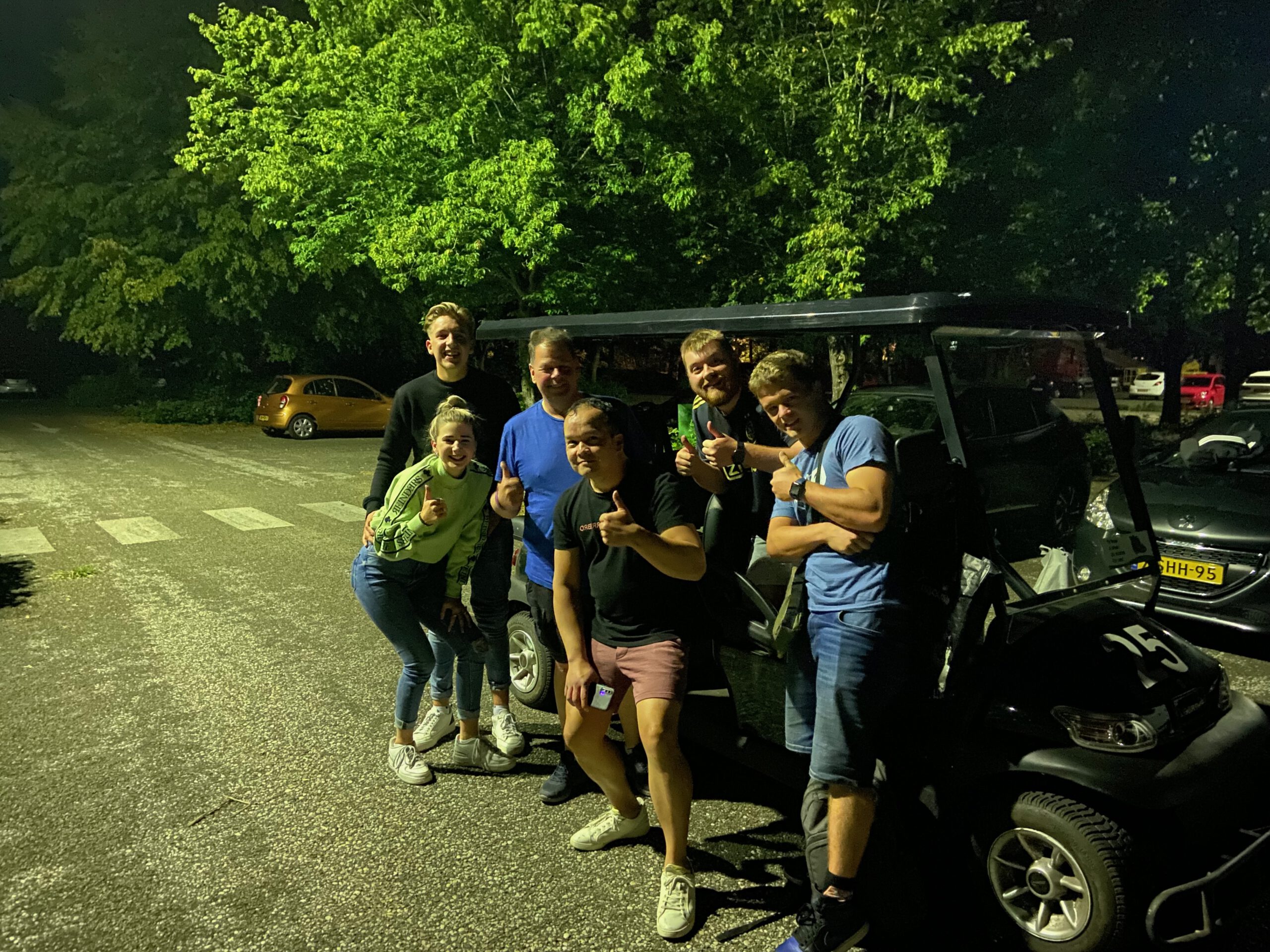 Center Parcs De Huttenheugte Day Visit night photo at parking area D with Chris and Rogier from AMFVLOGS, Peter Smit, Timo van den Berg, Timeuw, together with Floor and Tim, posing next to a golf cart under trees in Dalen, Drenthe after an evening at the Action Factory.