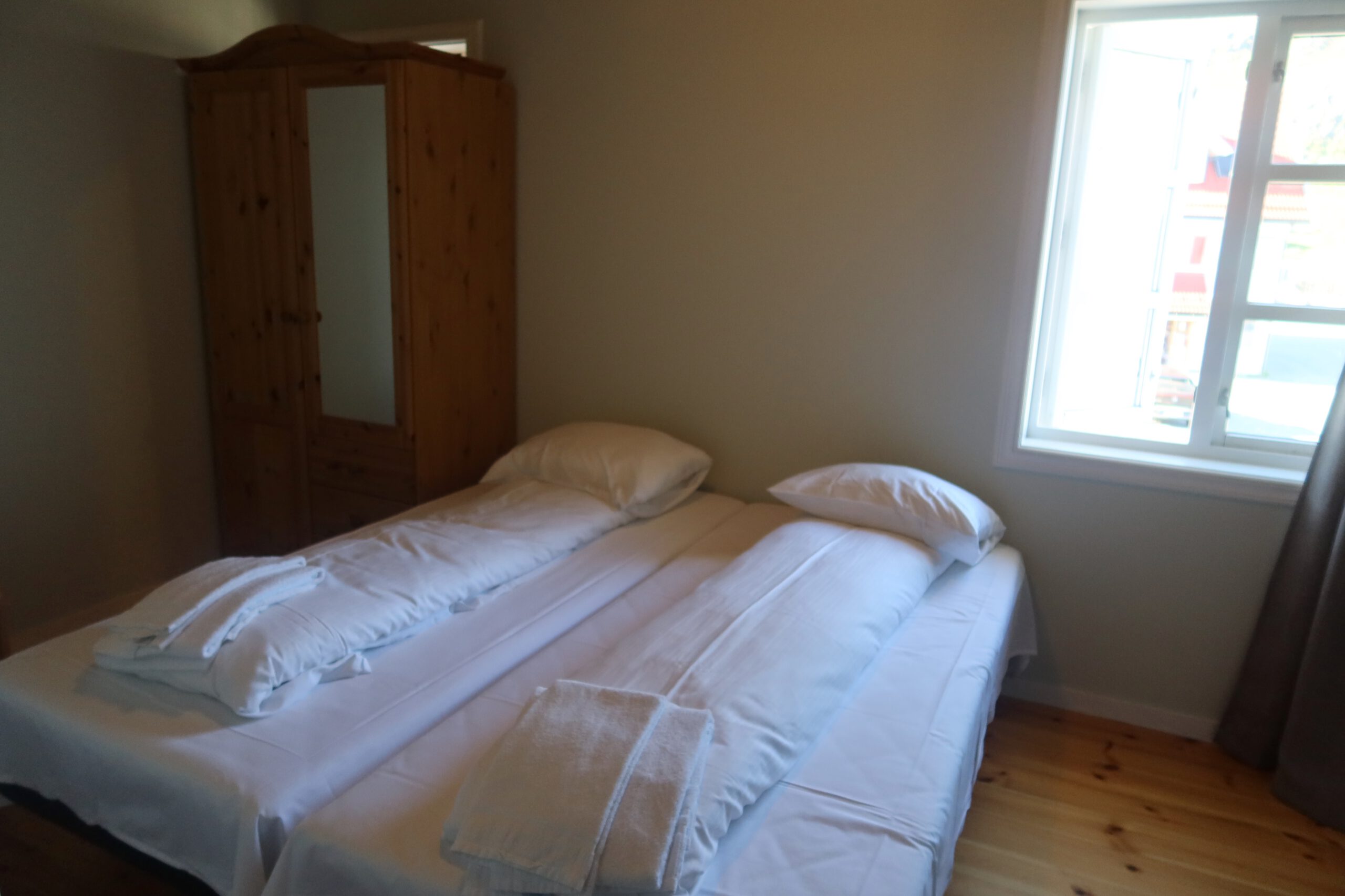 Simple double bedroom with white bedding, wooden floor and natural light in a Norwegian coastal guesthouse