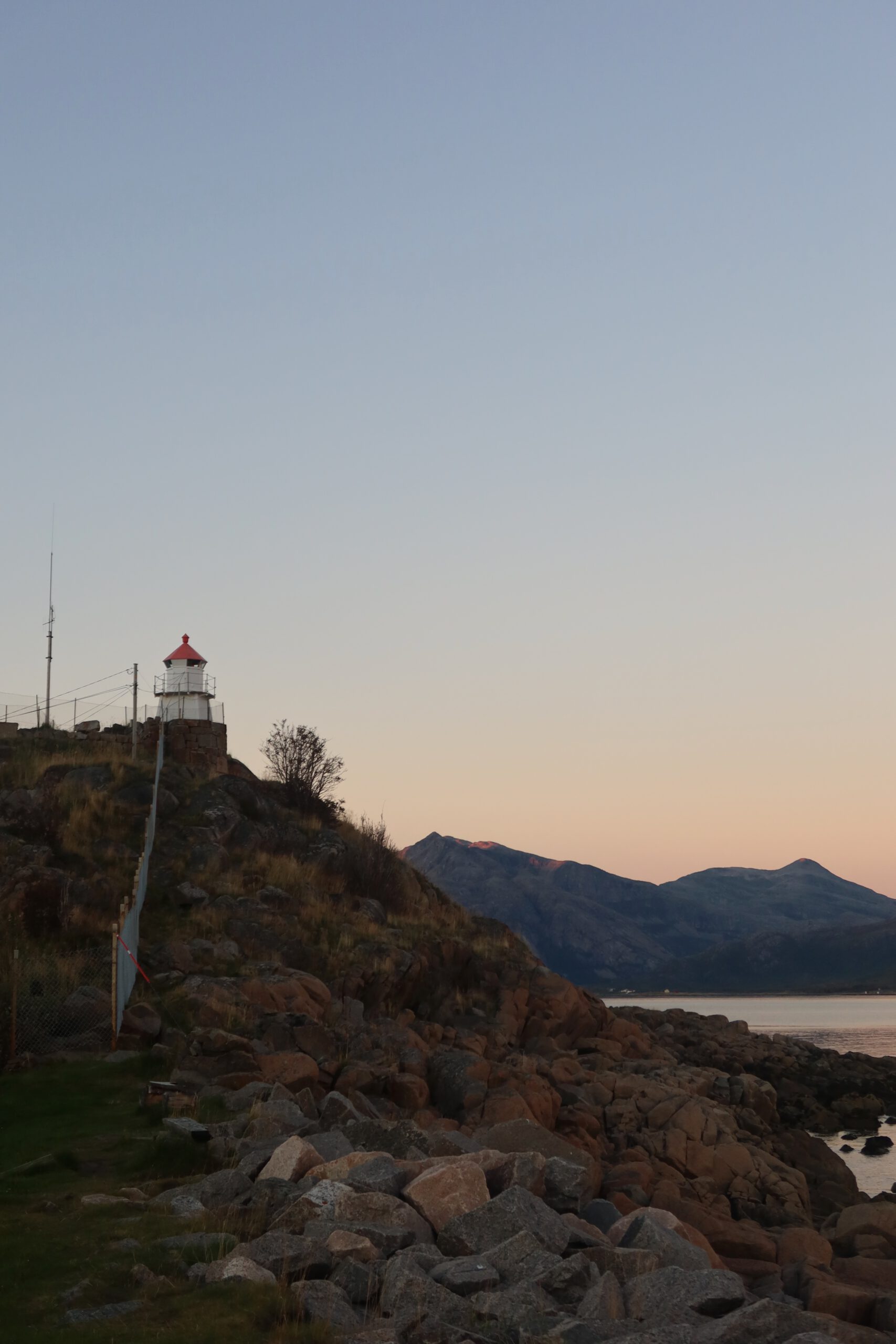 Hjortholmen Northern Lights Spot featuring the Lødingen lighthouse on a rocky coastline at dusk, with mountains, sea, and minimal light pollution in Northern Norway