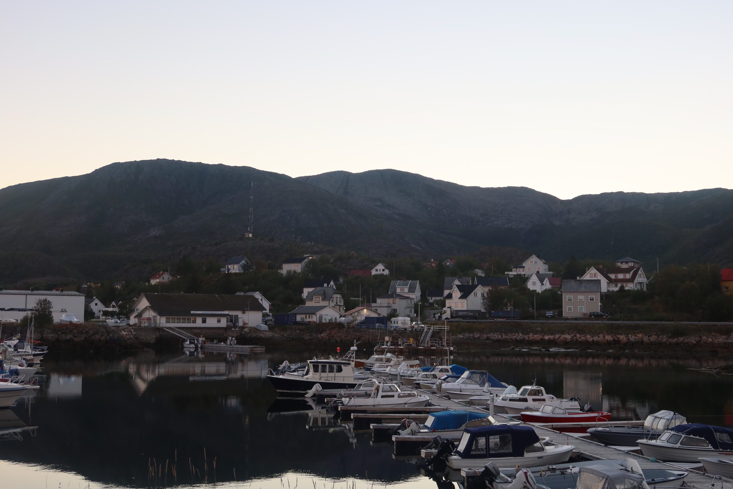 Harbor view in Lødingen Norway with small boats, calm water reflections and mountains rising behind the coastal village
