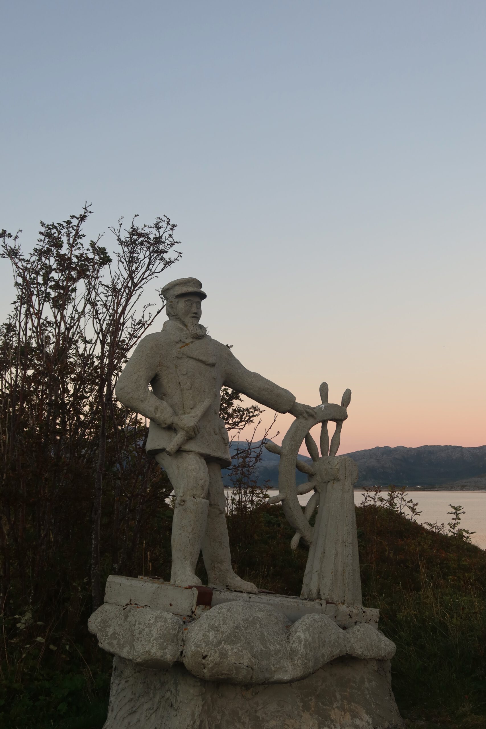 Hjortholmen Northern Lights Spot showing a historic coastal statue near Lødingen during calm evening light, overlooking the sea and surrounding Arctic landscape