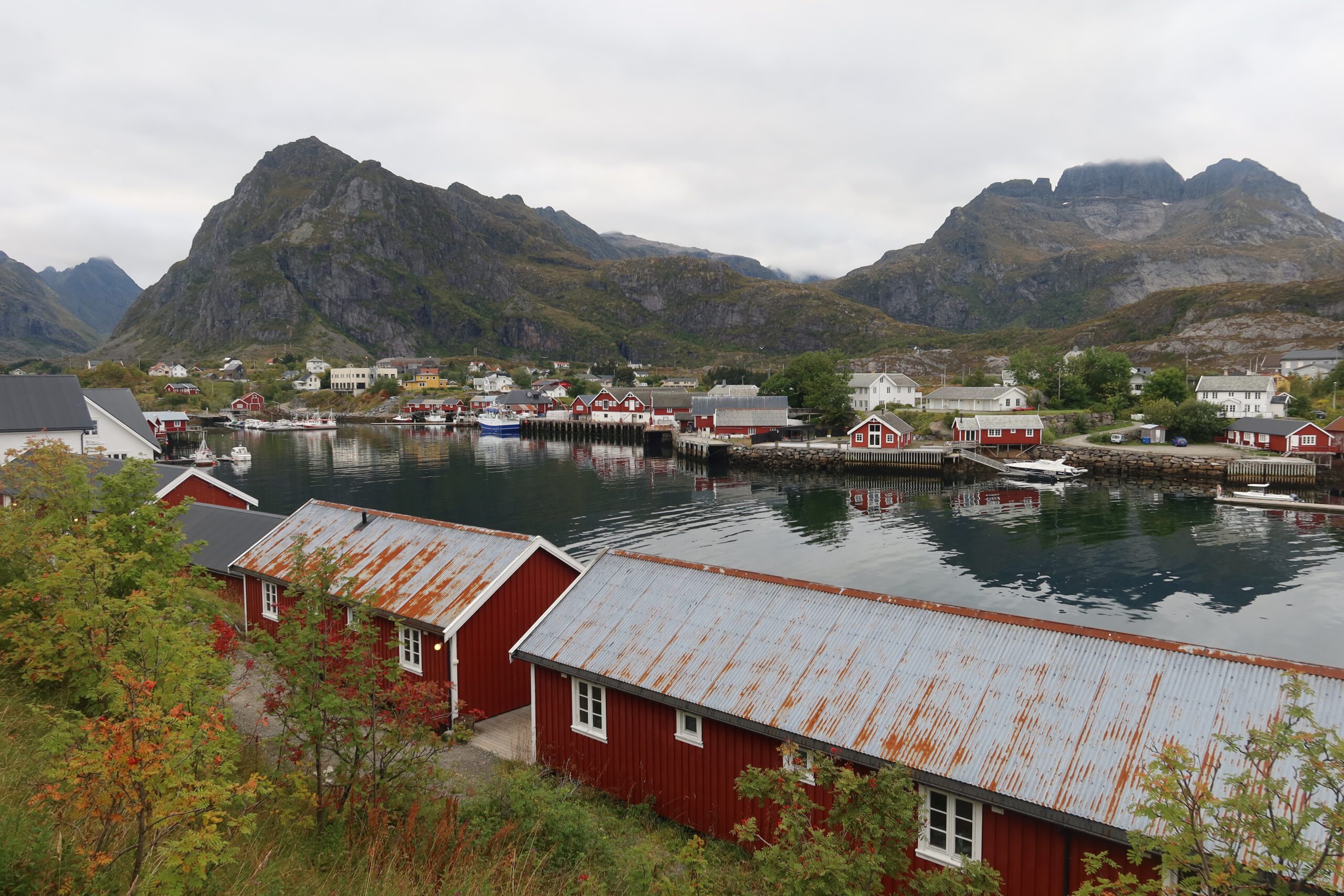 Harbor view of The Tide Fisherman Cabins Sørvågen, red traditional fisherman cabins along the waterfront with dramatic Lofoten mountains in the background, Sørvågen, Norway