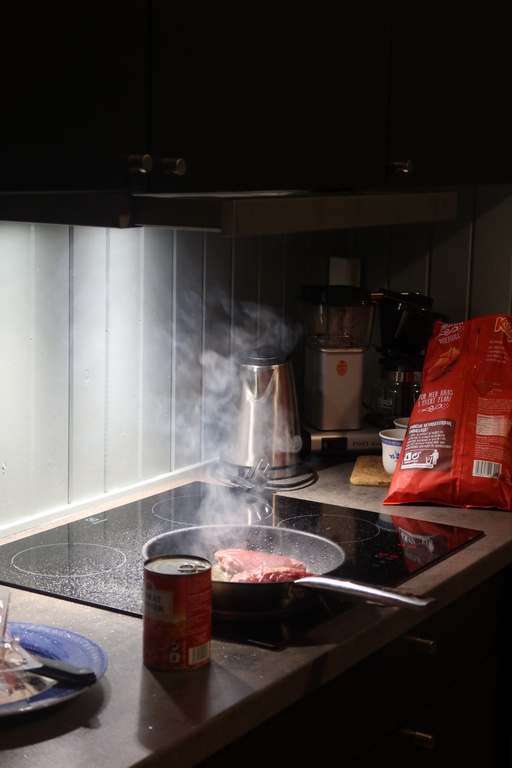The Tide Fisherman Cabins Lofoten, cooking fresh meat on the modern induction stove inside the fisherman cabin kitchen in Sørvågen