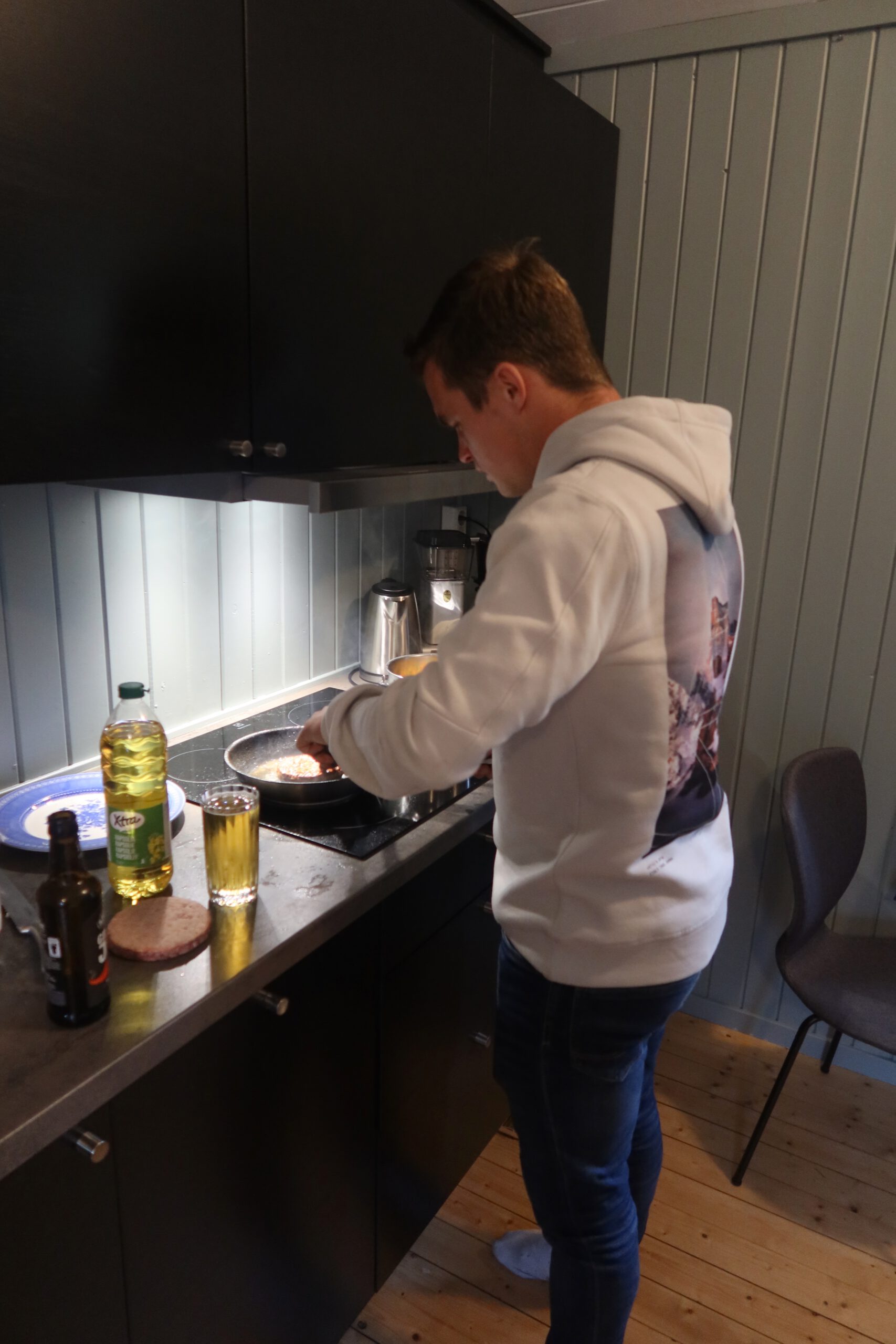 Peter Smit cooking dinner in the cabin kitchen on the Lofoten Islands, preparing fresh food on the stovetop inside a modern Scandinavian fisherman cabin