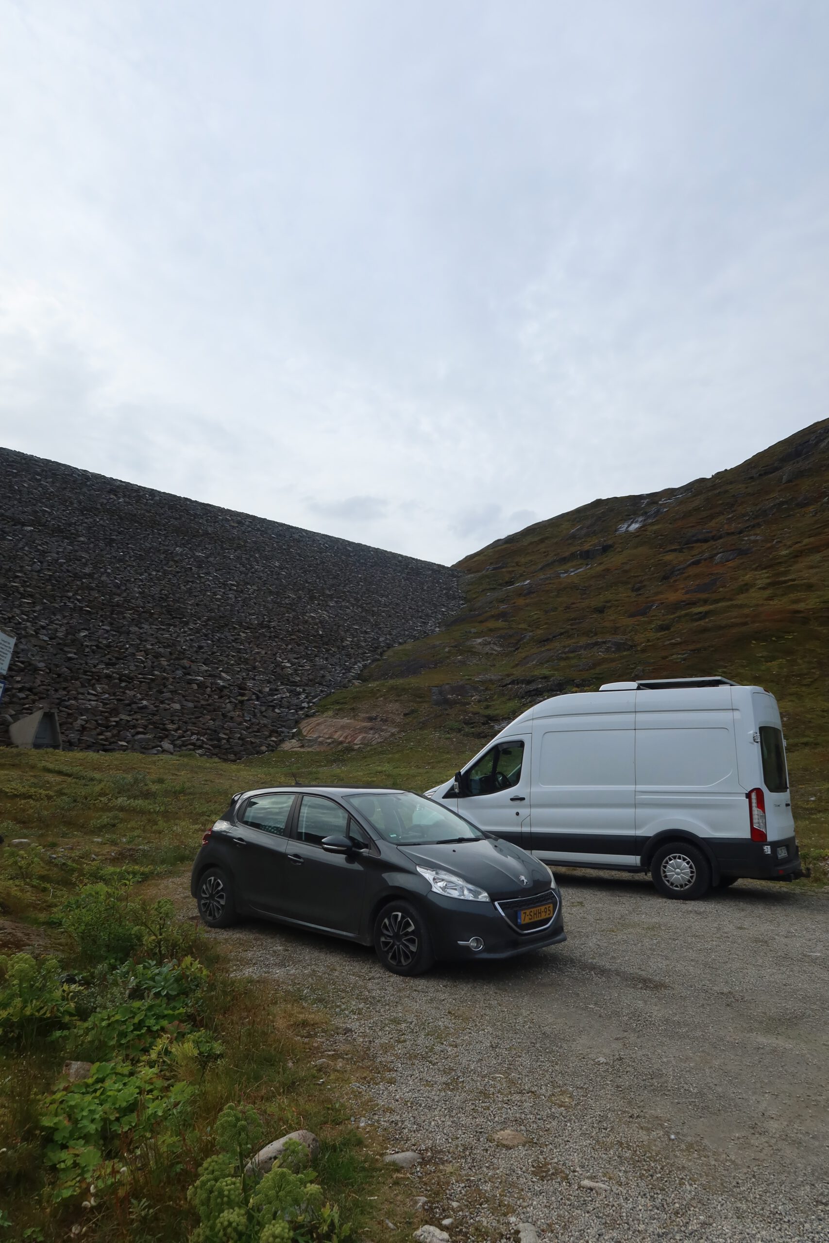 Gulbrakka Basecamp Glomfjord road trip stop, Peugeot 208 and white camper van parked near a mountain dam along a remote gravel road in Northern Norway