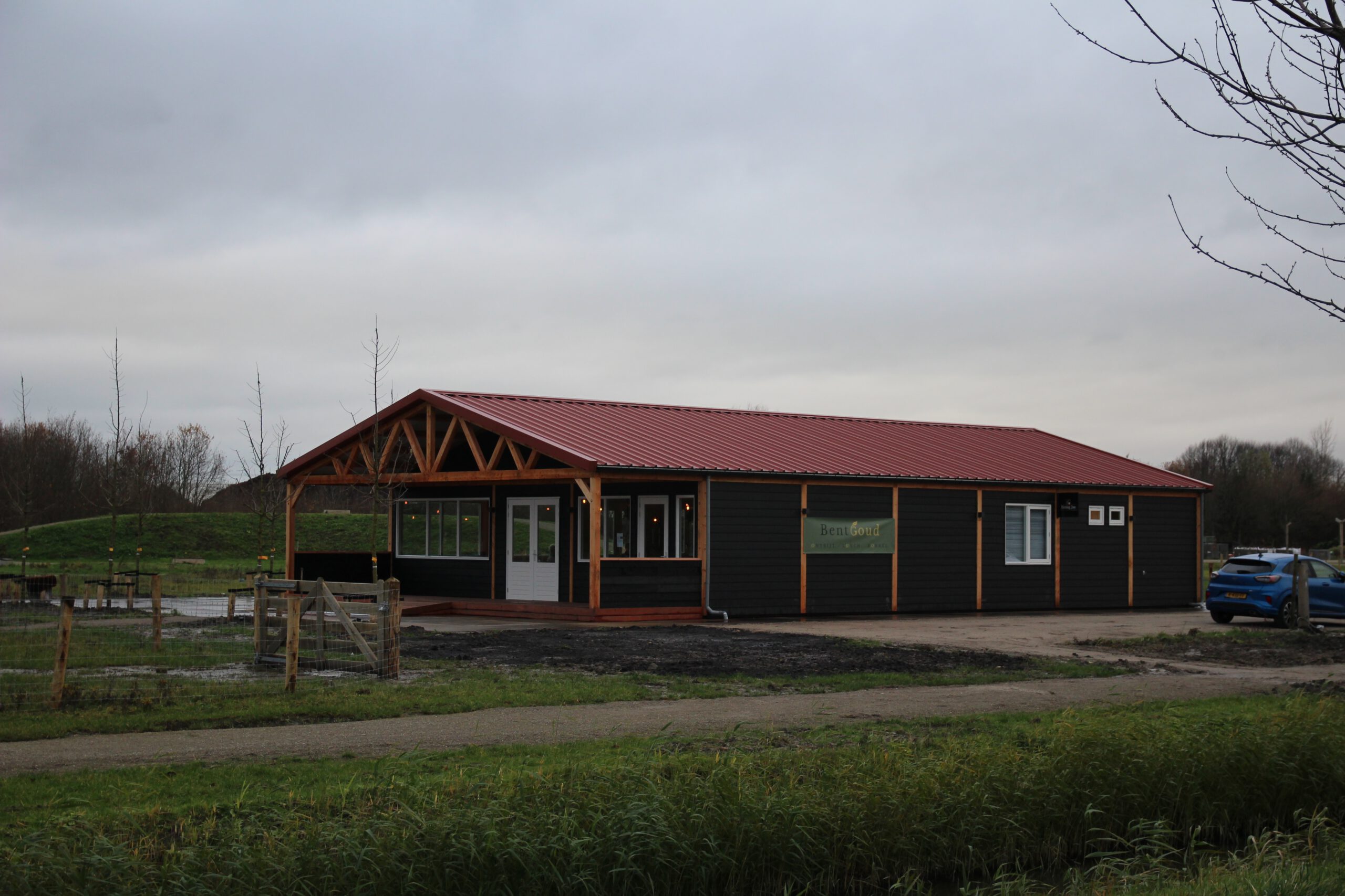 Wide exterior view of BentGoud Bentwoud showing the modern wooden restaurant building with red roof, parking area, and surrounding Bentwoud landscape