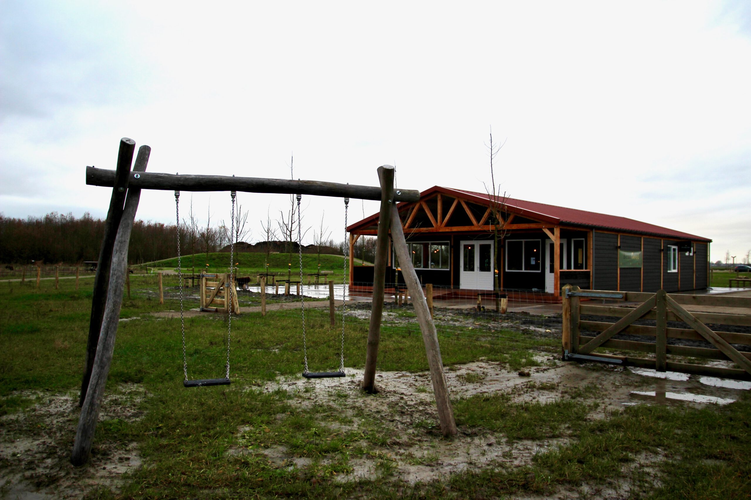 Exterior view of BentGoud Bentwoud with the restaurant building, playground swings, and open green landscape at the entrance of the Bentwoud nature area
