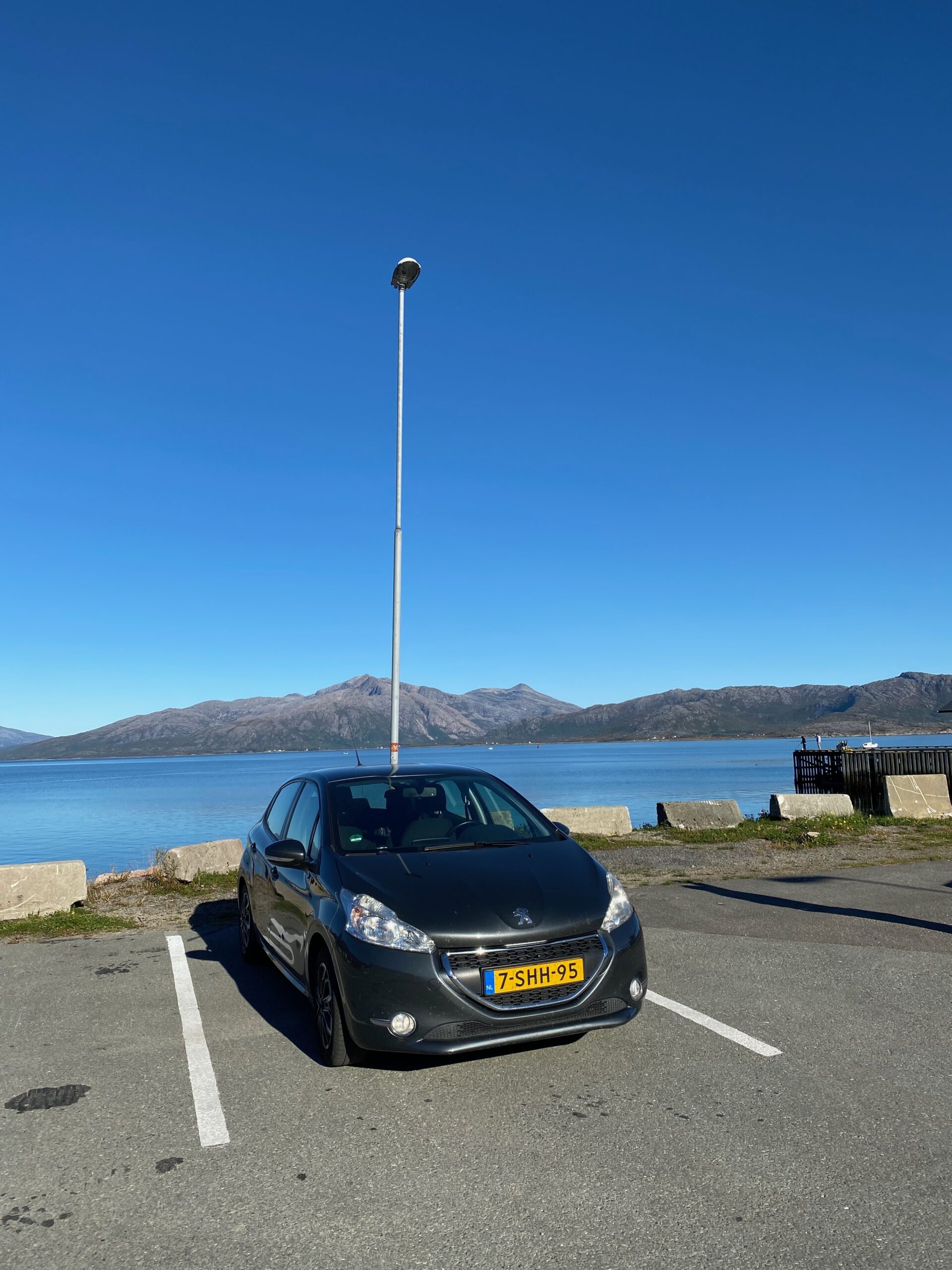 Road trip car parked near Lødingen Brygge Hotel Norway, car by the fjord with mountains and clear blue sky in Northern Norway