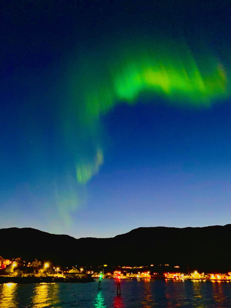 Strong aurora borealis over Hjertholmen island near Lødingen, dramatic northern lights dancing above the mountains and sea in Northern Norway