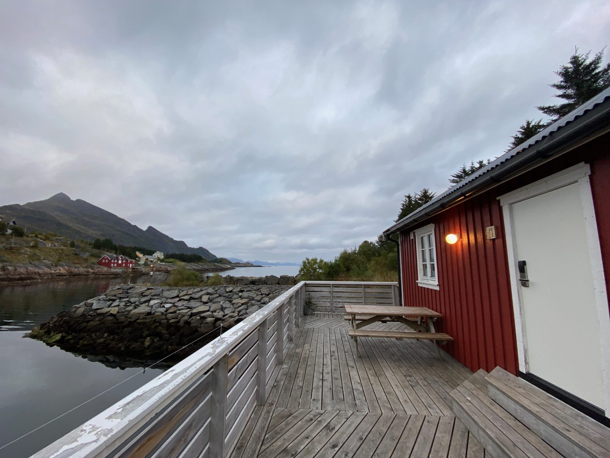 The Tide Fisherman Cabins Sørvågen private wooden terrace with picnic table, red rorbu cabin and quiet coastal surroundings in the Lofoten Islands