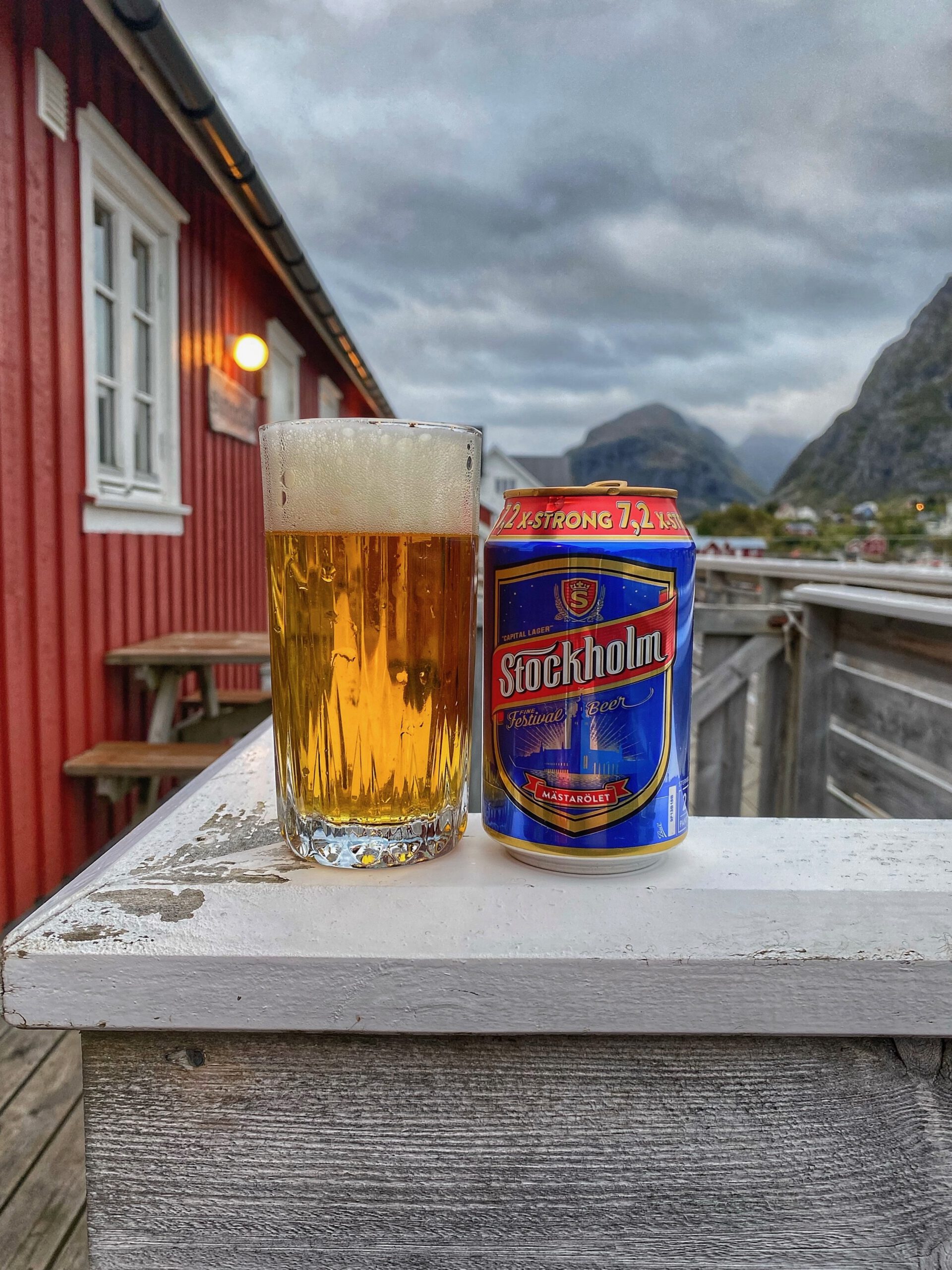 The Tide Lofoten fisherman cabins evening terrace scene with Stockholm lager beer, red fishermen cabins and mountains in the background