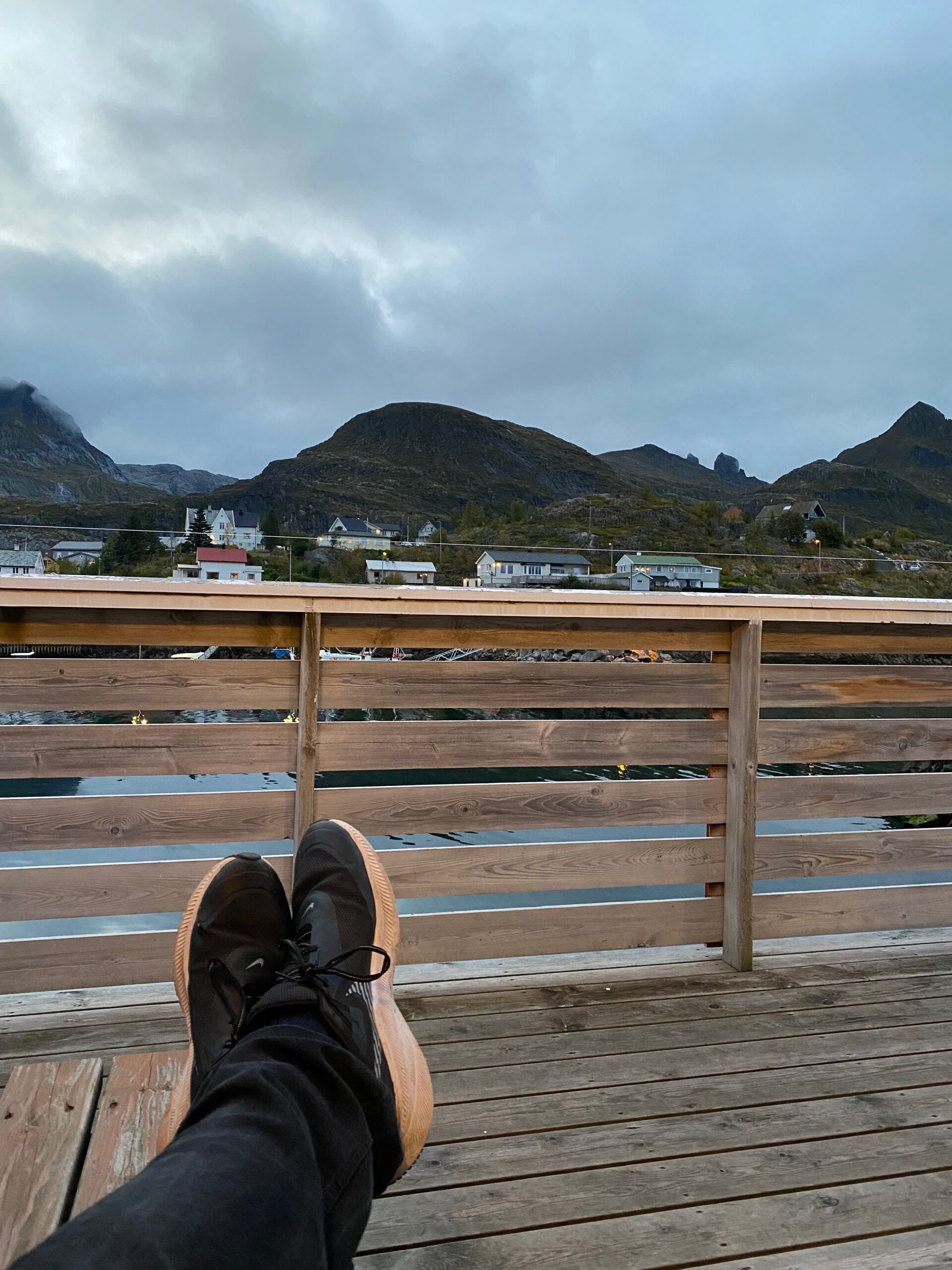The Tide Lofoten fisherman cabins terrace view with mountains and calm harbor, relaxing moment from the wooden deck in Sørvågen
