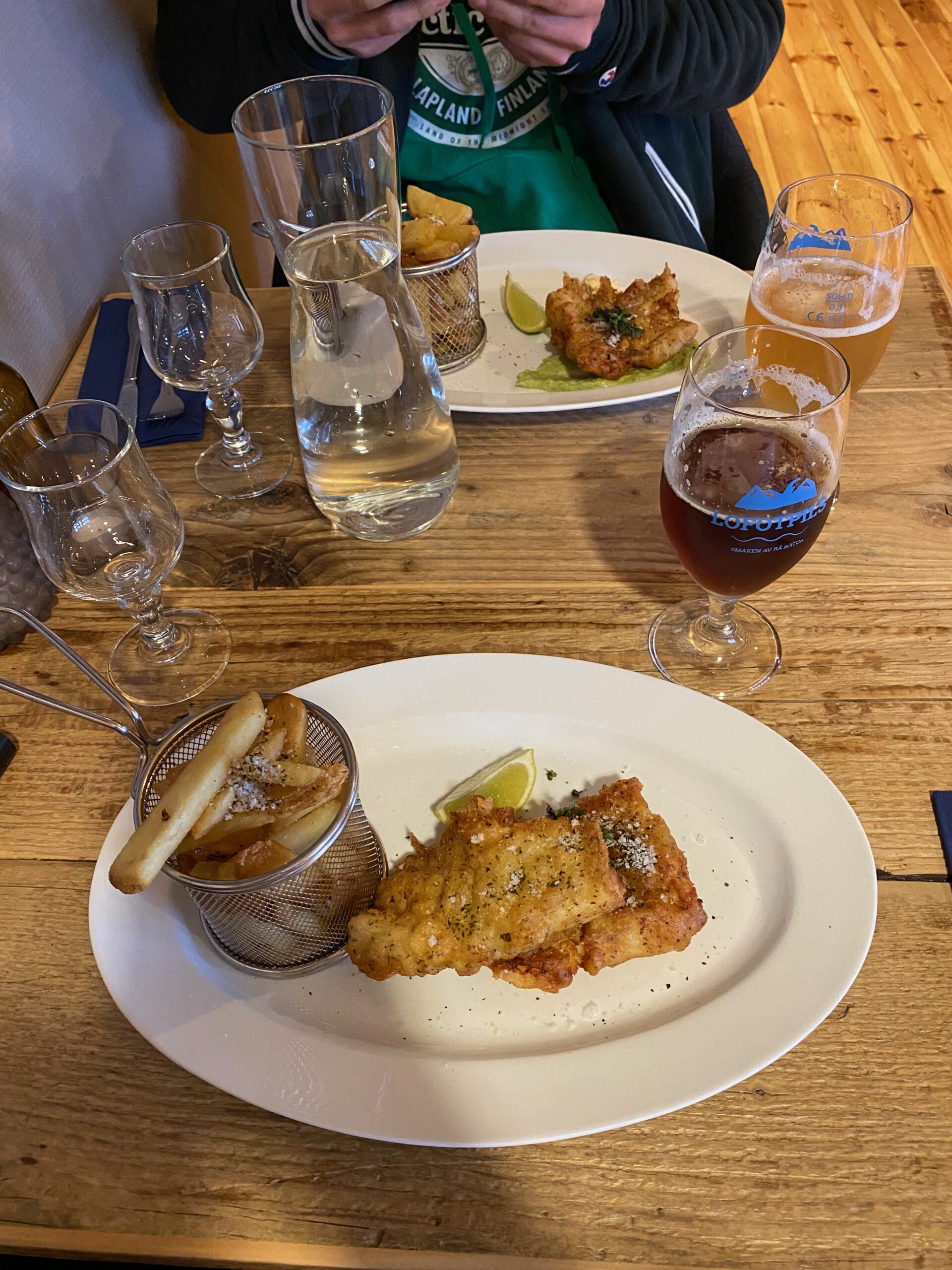 Å Rorbuer Lofoten restaurant fish and chips served with crispy fries and local Lofoten beer on a wooden table in Å i Lofoten Norway