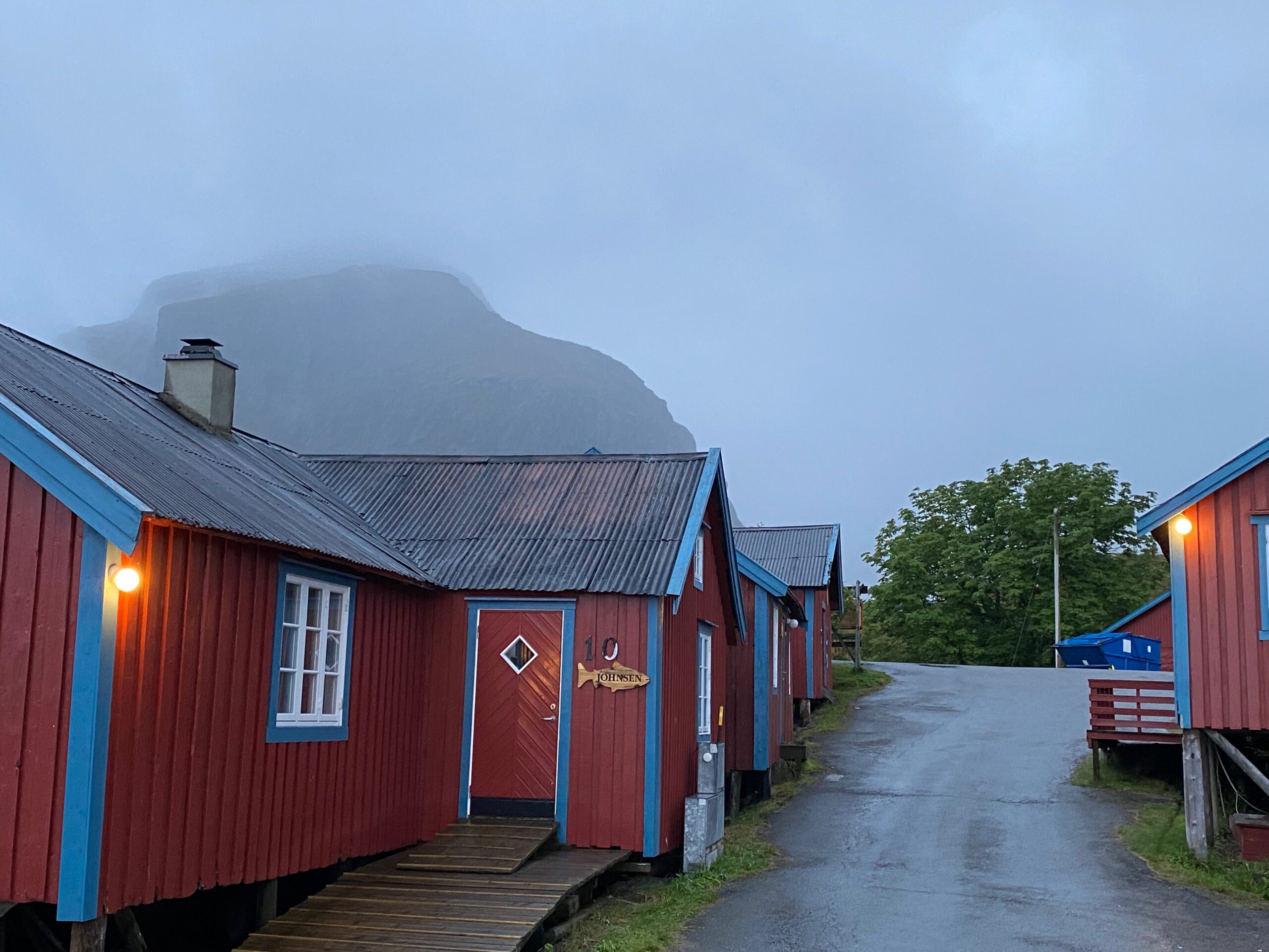 Å Rorbuer Lofoten traditional red fishing cabins lined along the path with misty mountains in the background in Å i Lofoten Norway