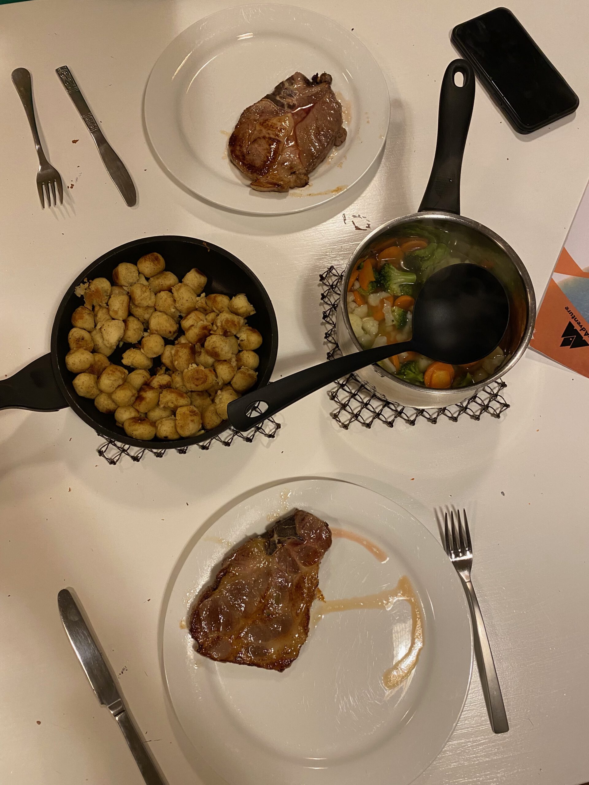 Gulbrakka Basecamp Glomfjord communal dinner overview, plates with grilled steak, pan fried potatoes and boiled vegetables, served in the shared kitchen after a long travel day in Northern Norway