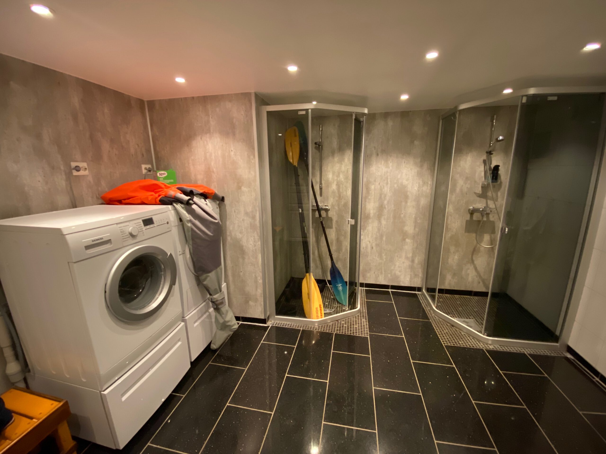 Gulbrakka Basecamp Glomfjord shared bathroom facilities, clean basement bathroom with multiple shower cabins, washing machine, drying area and tiled walls for guests