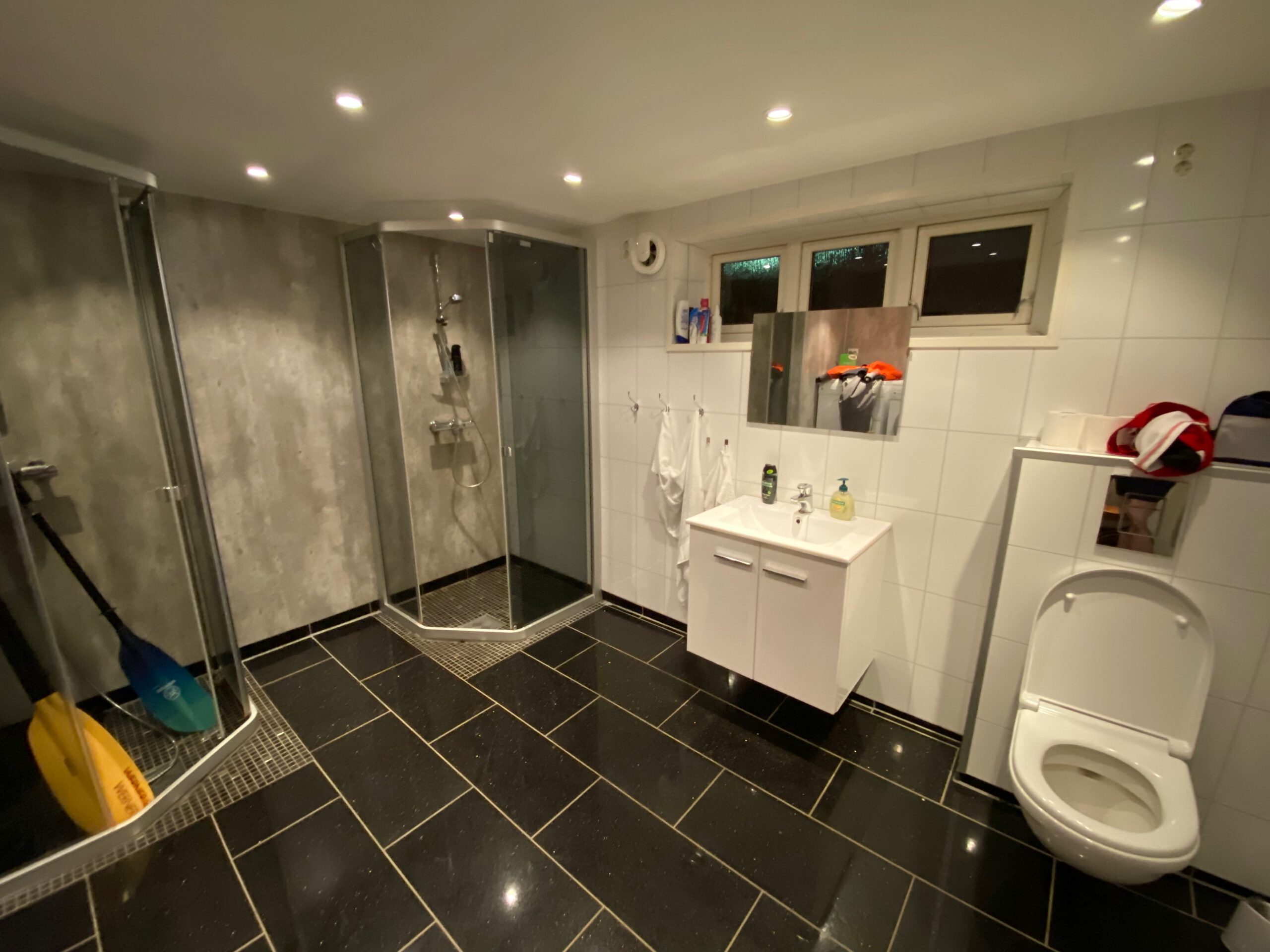 Gulbrakka Basecamp Glomfjord shared bathroom, modern communal bathroom with tiled floor, double shower cabins, sink, mirror and toilet in the basement area