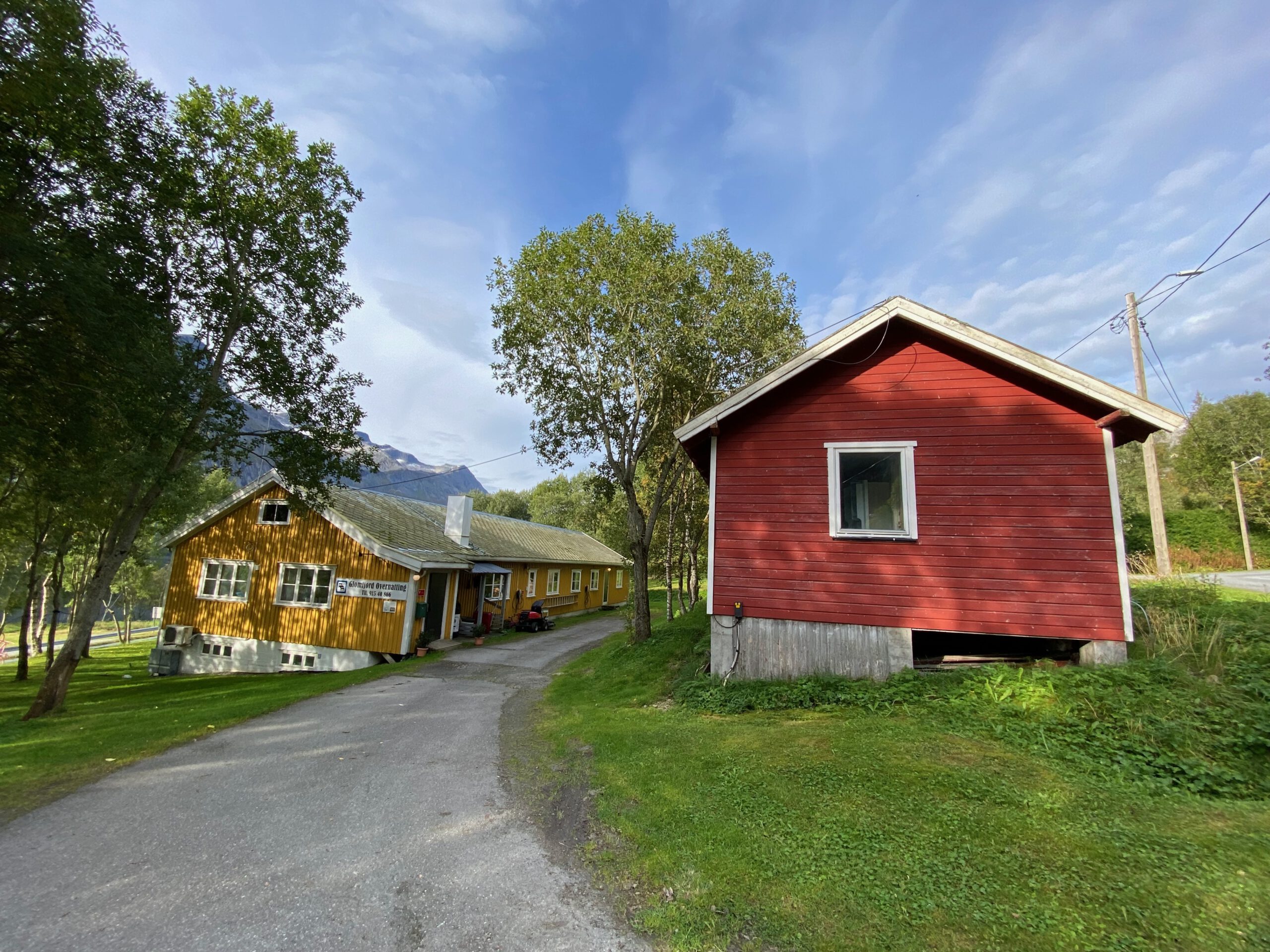 Gulbrakka Basecamp Glomfjord exterior overview, traditional yellow and red wooden basecamp buildings surrounded by trees and mountains in Northern Norway