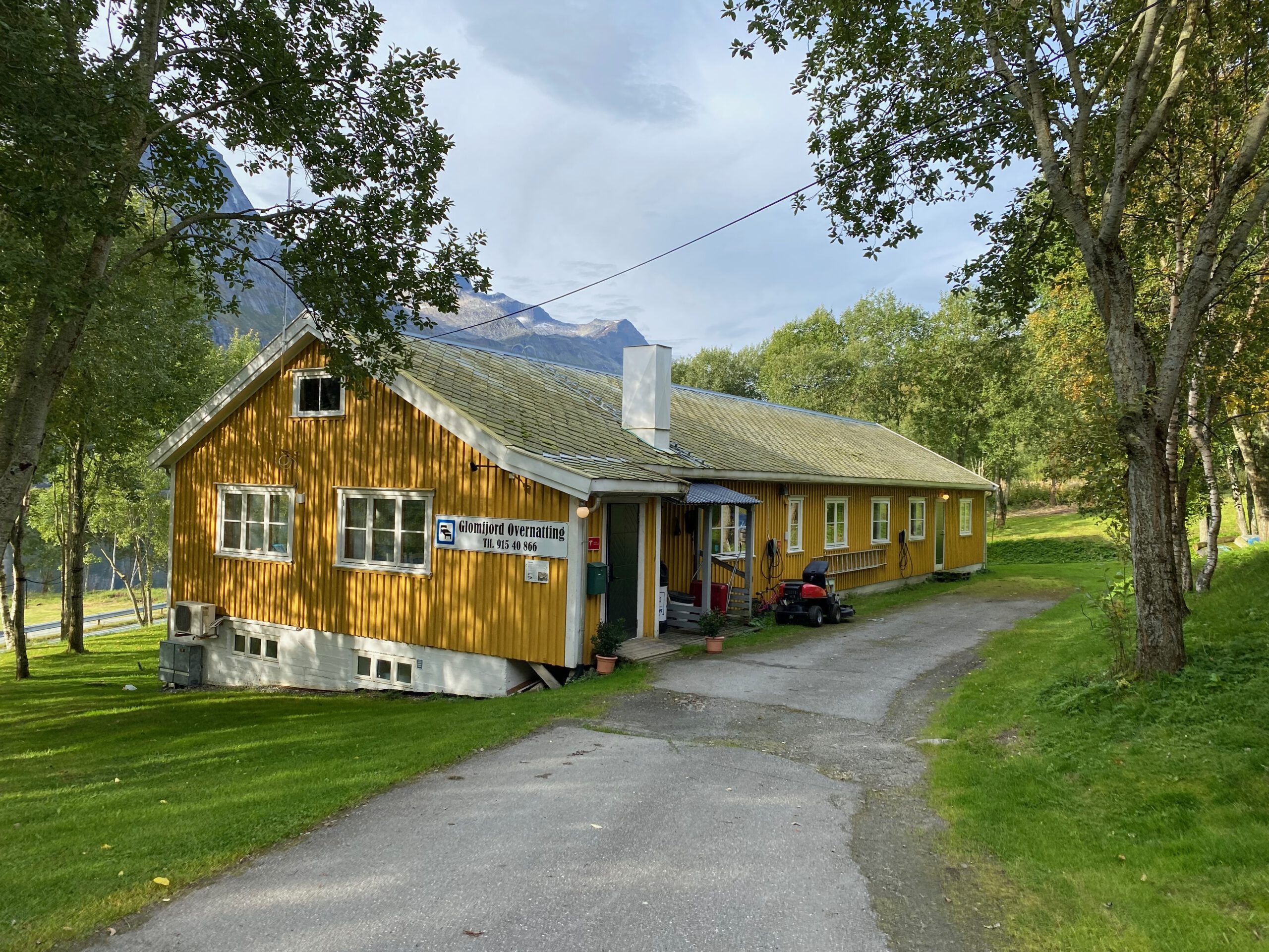 Gulbrakka Basecamp Glomfjord exterior view, traditional yellow basecamp surrounded by trees and mountains in Northern Norway, peaceful accommodation near nature and hiking routes