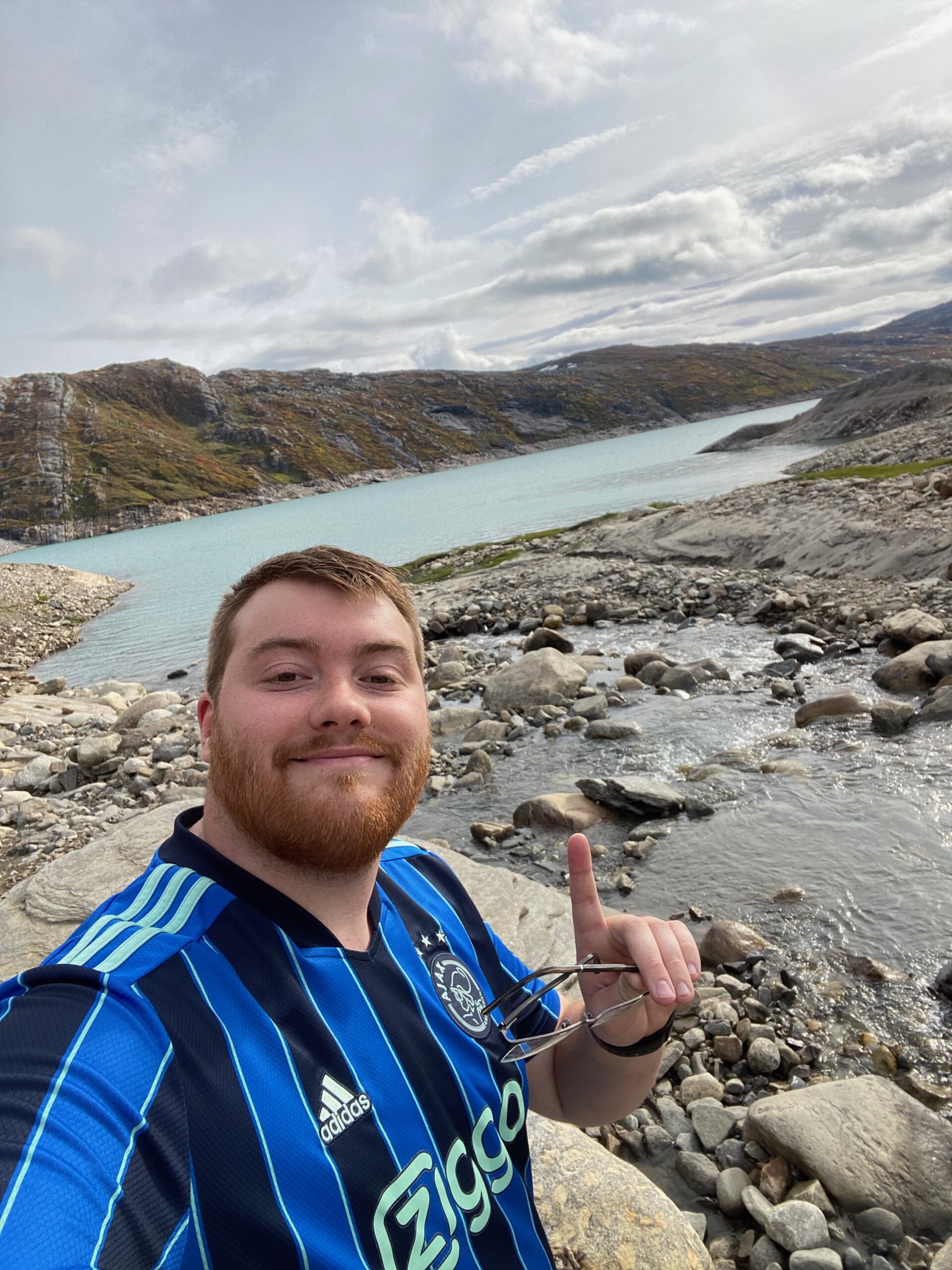 Glomfjord lake and dam adventure with Timo van den Berg, Timeuw, standing beside a glacier fed stream with turquoise Storglomvatnet and Arctic mountains in the background