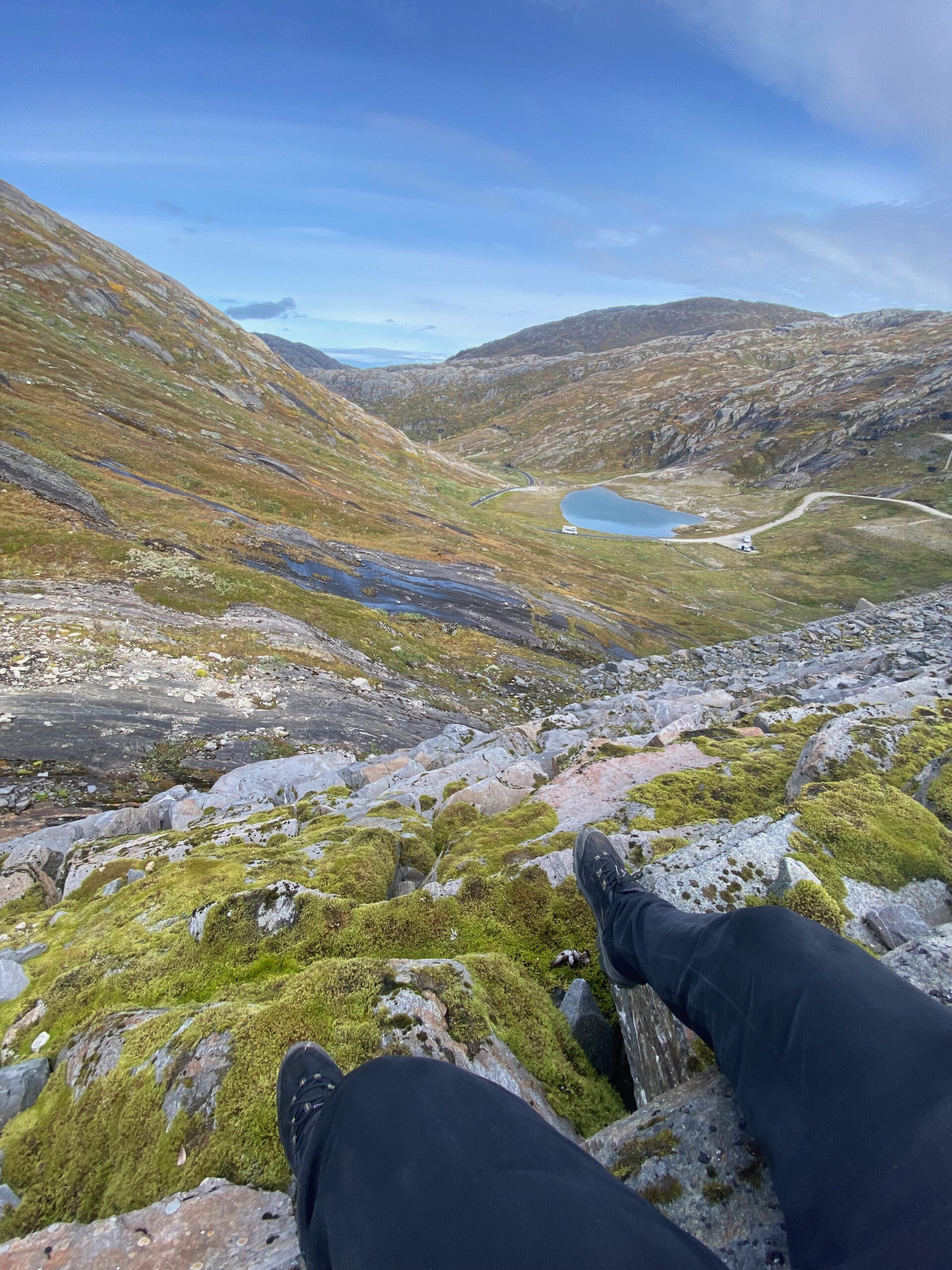 View over Storglomvatnet from a rocky hiking viewpoint, looking down into the valley with alpine terrain and winding mountain roads