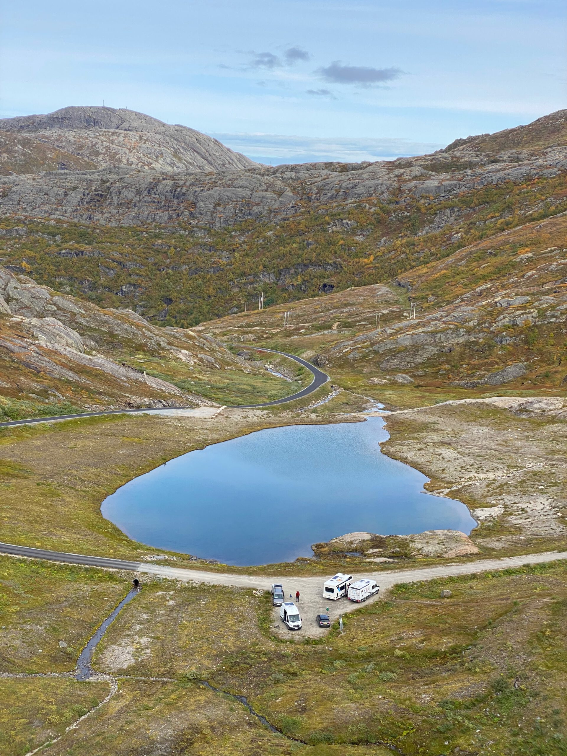 Glomfjord lake and dam adventure showing a winding mountain road, small alpine lake, parked campers and rugged terrain near Storglomvatnet in Northern Norway