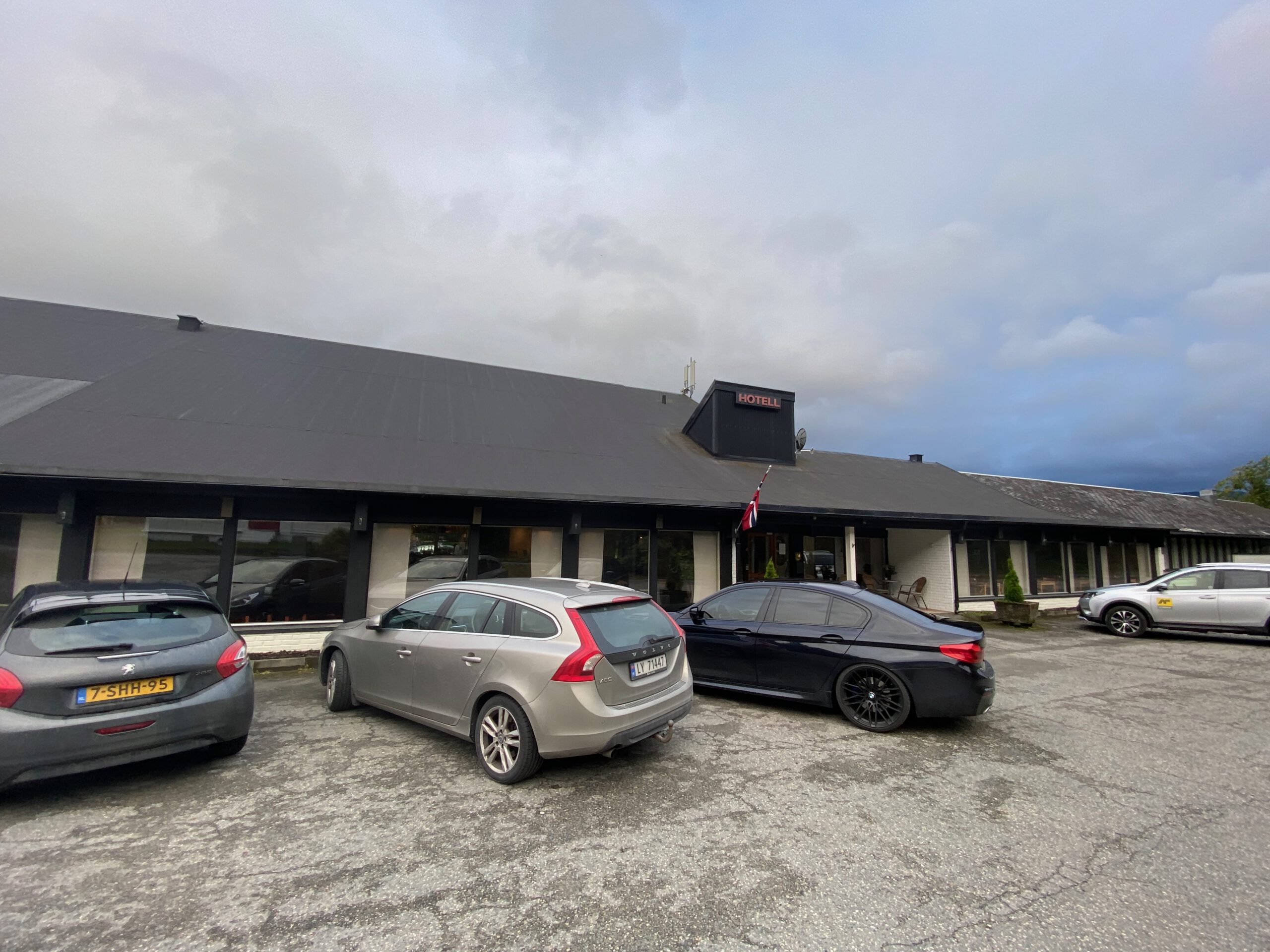 Støren Hotel Norway review exterior view with free parking in Trøndelag, showing the hotel facade and parking area with a Peugeot 208, Volvo V60, BMW 5 Series and another Volvo parked in front near the E6 road trip route