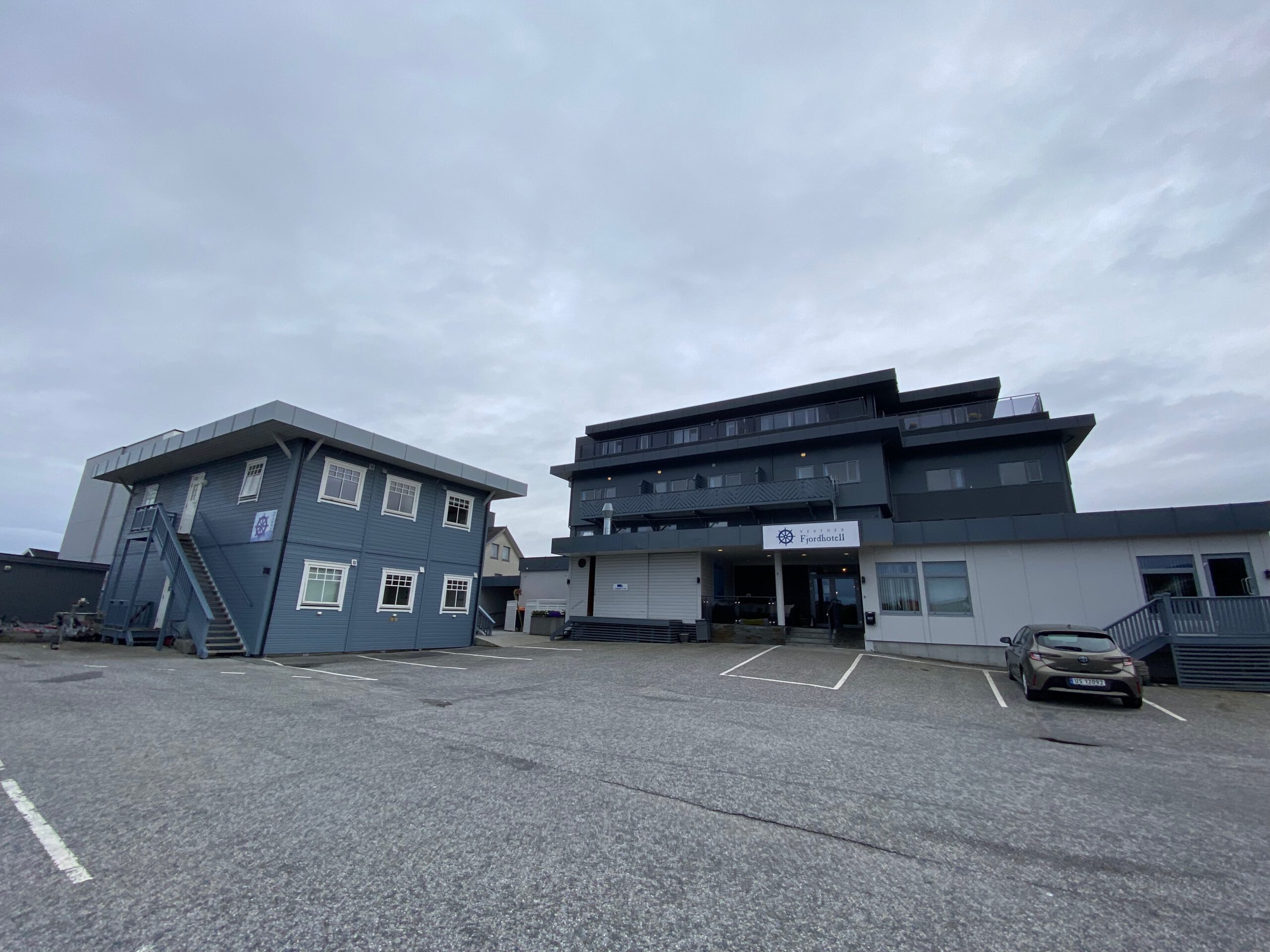 Vestnes Fjordhotel exterior view with parking area, main building, annex structure, and cloudy fjord sky in Vestnes Norway