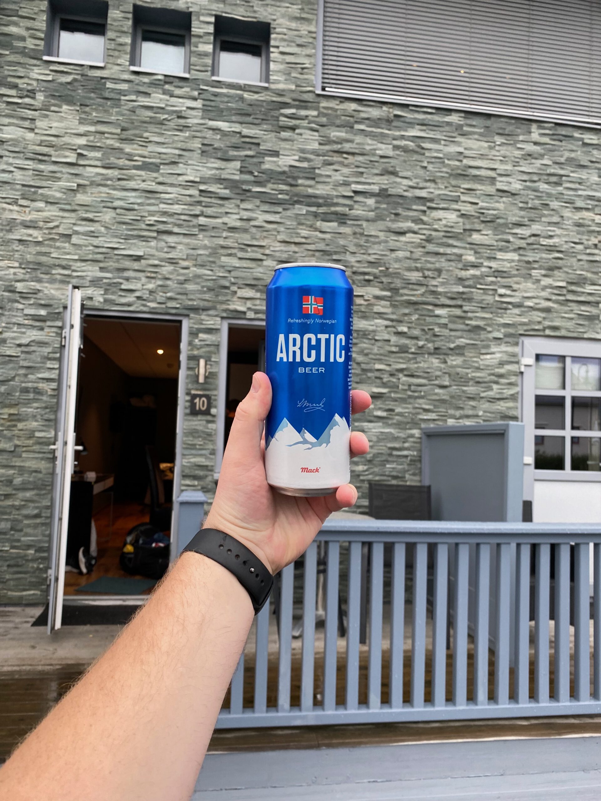 Mack Arctic Beer held in front of mini studio at Vestnes Fjordhotel with stone facade and terrace railing in Vestnes Norway
