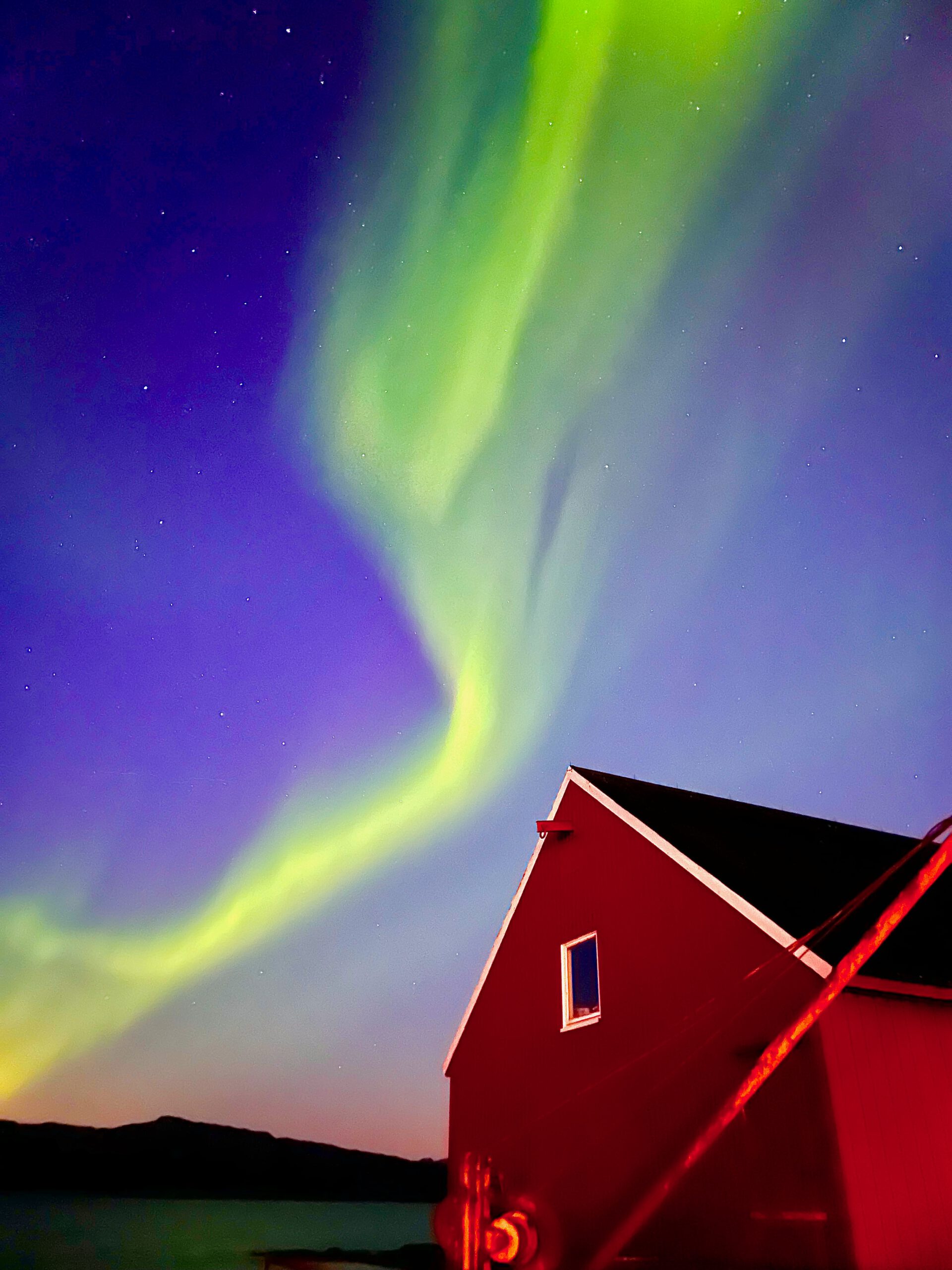 Northern Lights Lødingen Norway with intense green aurora curtains twisting above the fjord and distant shoreline lights under a clear Arctic sky