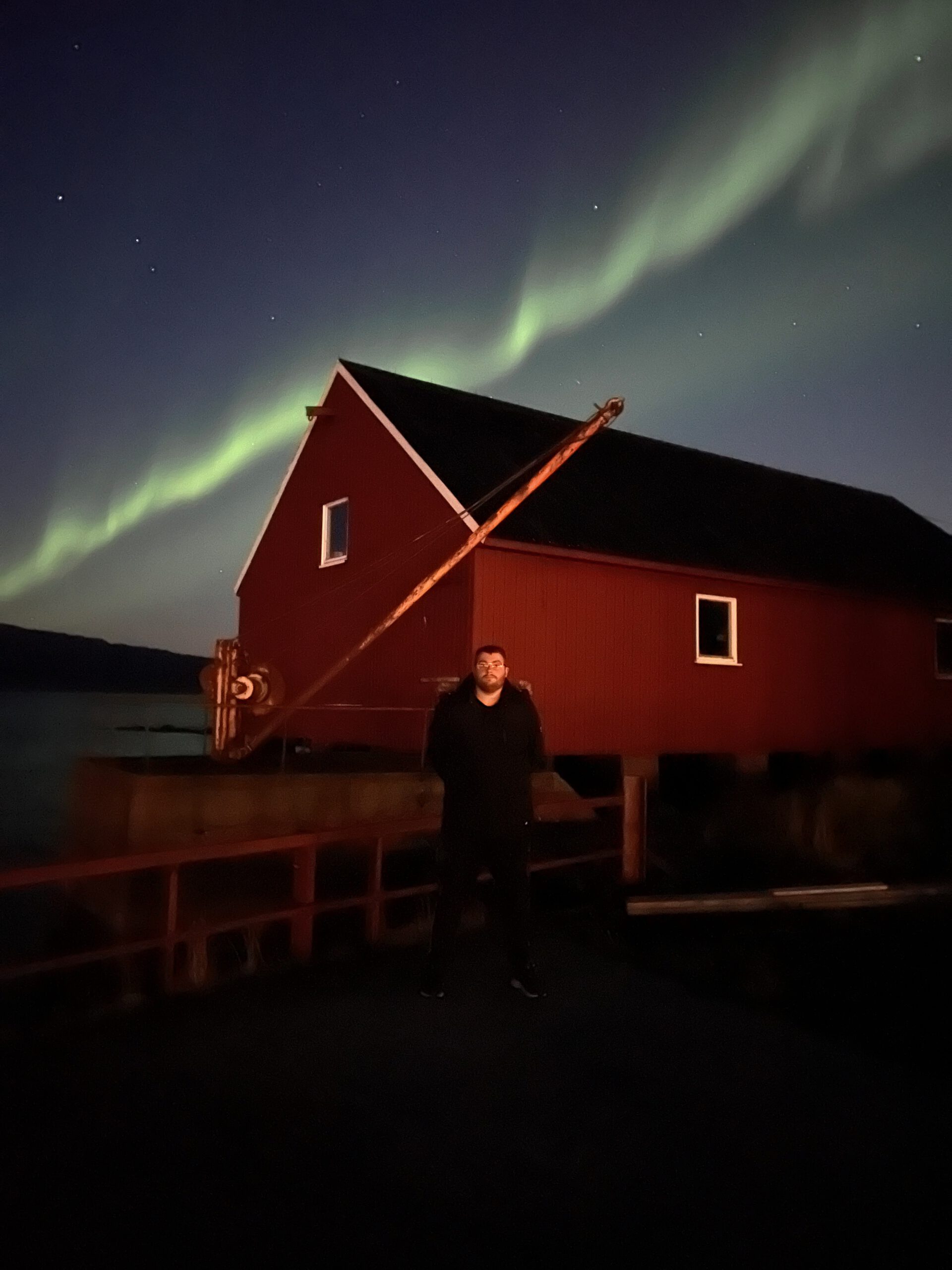 Hjertholmen Lødingen Northern Lights with photographer Timo van den Berg standing in front of a red boathouse under a clear Arctic sky