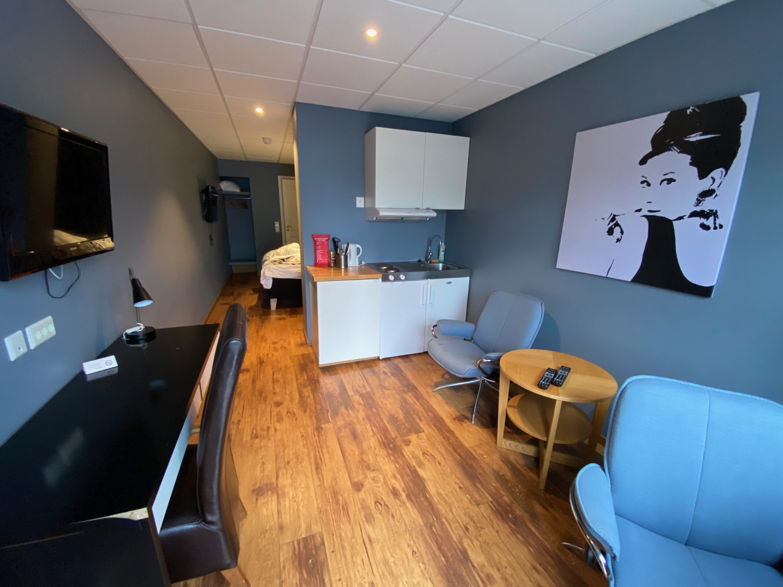 Mini studio living area at Vestnes Fjordhotel with kitchenette, seating area, desk, flat screen TV, and wooden flooring in Vestnes Norway