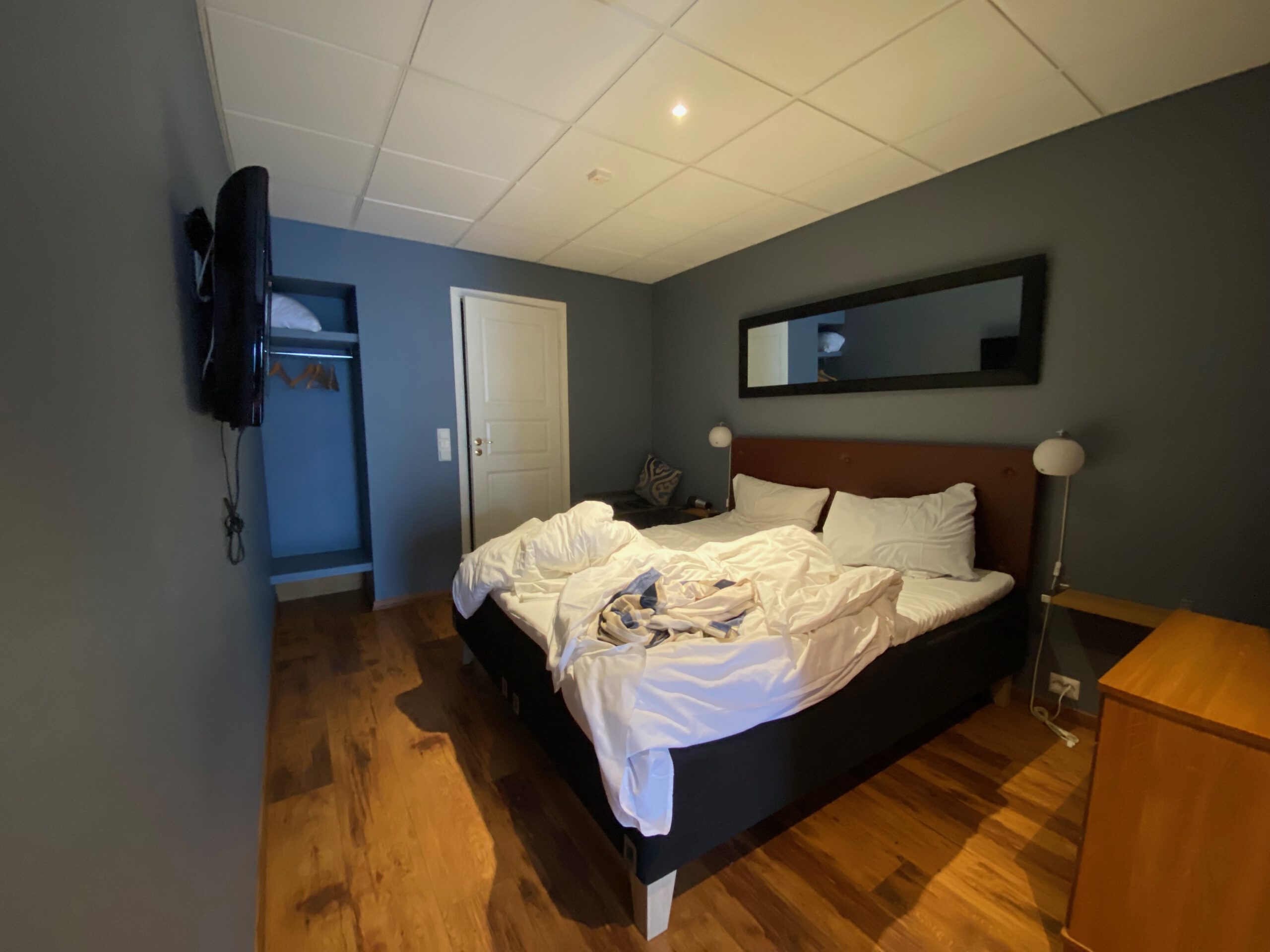 Bedroom inside mini studio at Vestnes Fjordhotel with double bed, wooden floor, wall mirror, and mounted television in Vestnes Norway