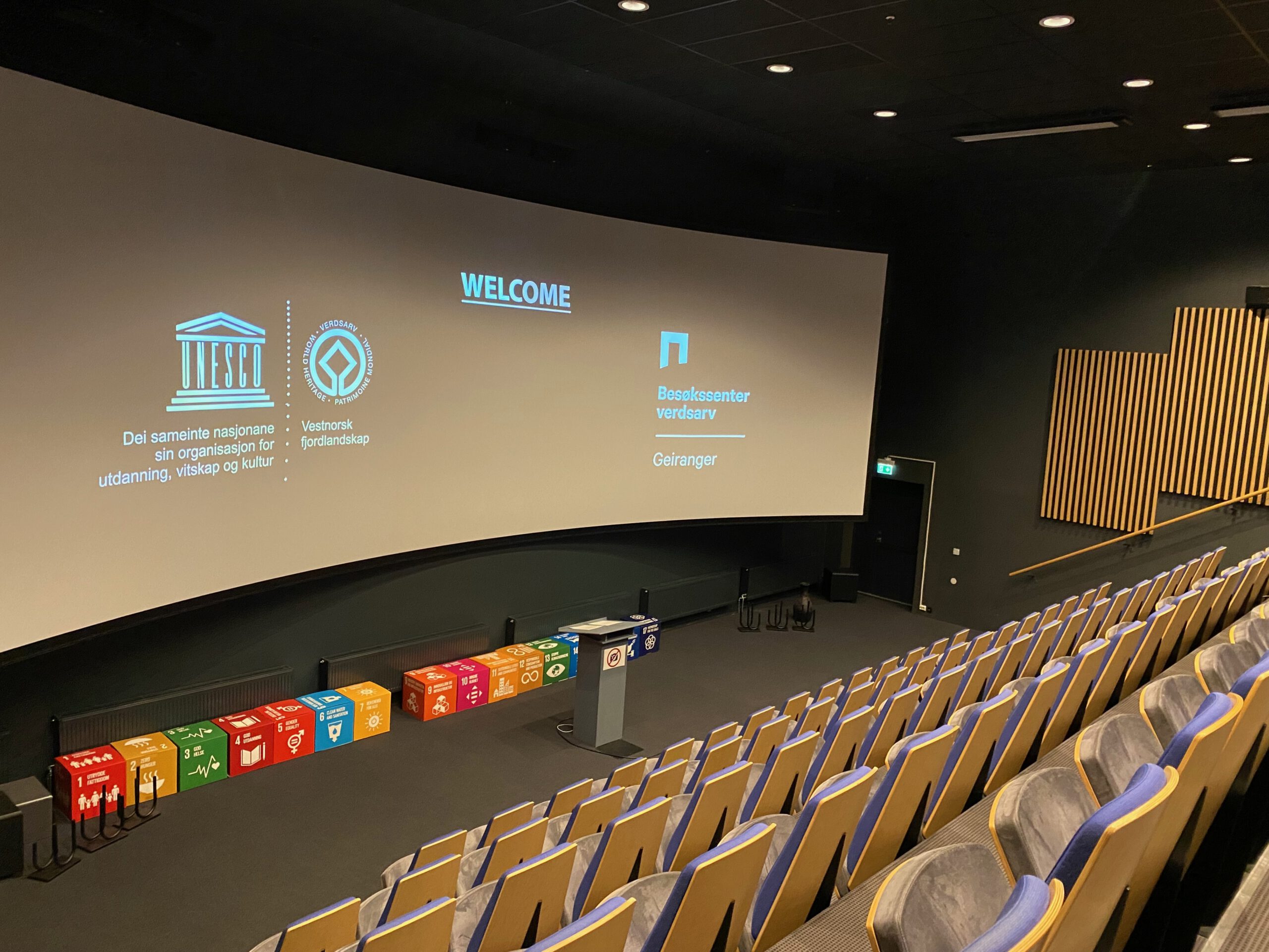 Norsk Fjordsenter Geiranger theater with large cinema screen showing UNESCO welcome film, modern auditorium with rows of seats inside the visitor center