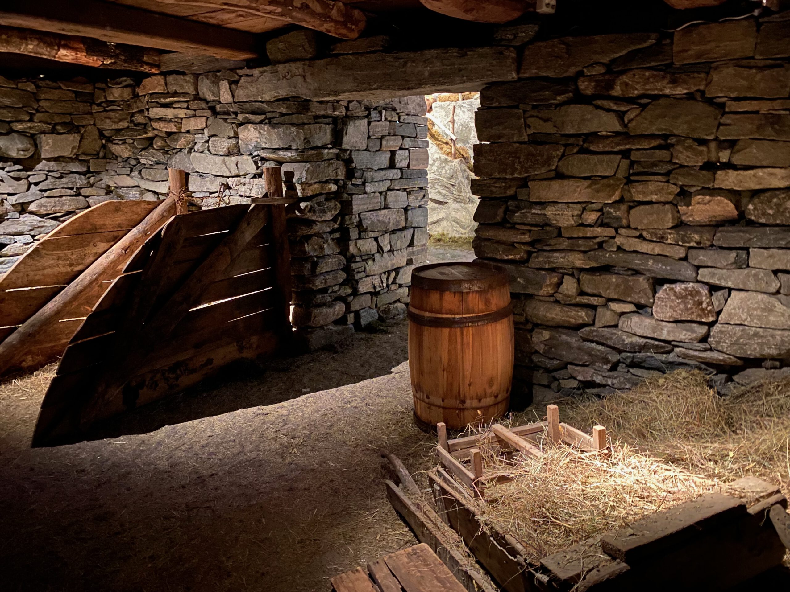 Stone barn interior reconstruction at Norsk Fjordsenter Geiranger with wooden gate, hay rack and barrel, showcasing traditional farming life in the UNESCO World Heritage Geirangerfjord region