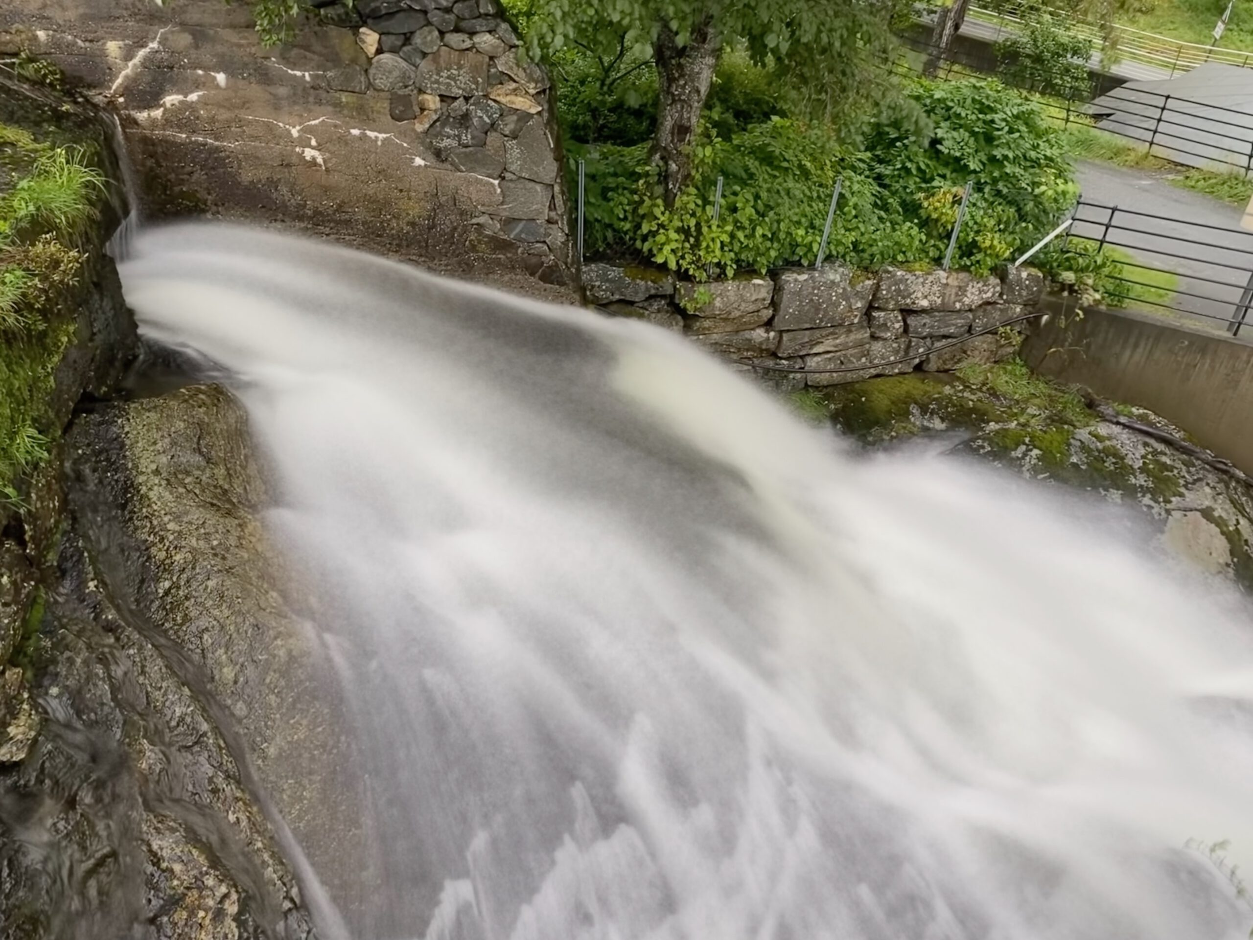 Close-up long exposure view of waterfall at Norsk Fjordsenter Geiranger with smooth flowing water over stone walls and green vegetation