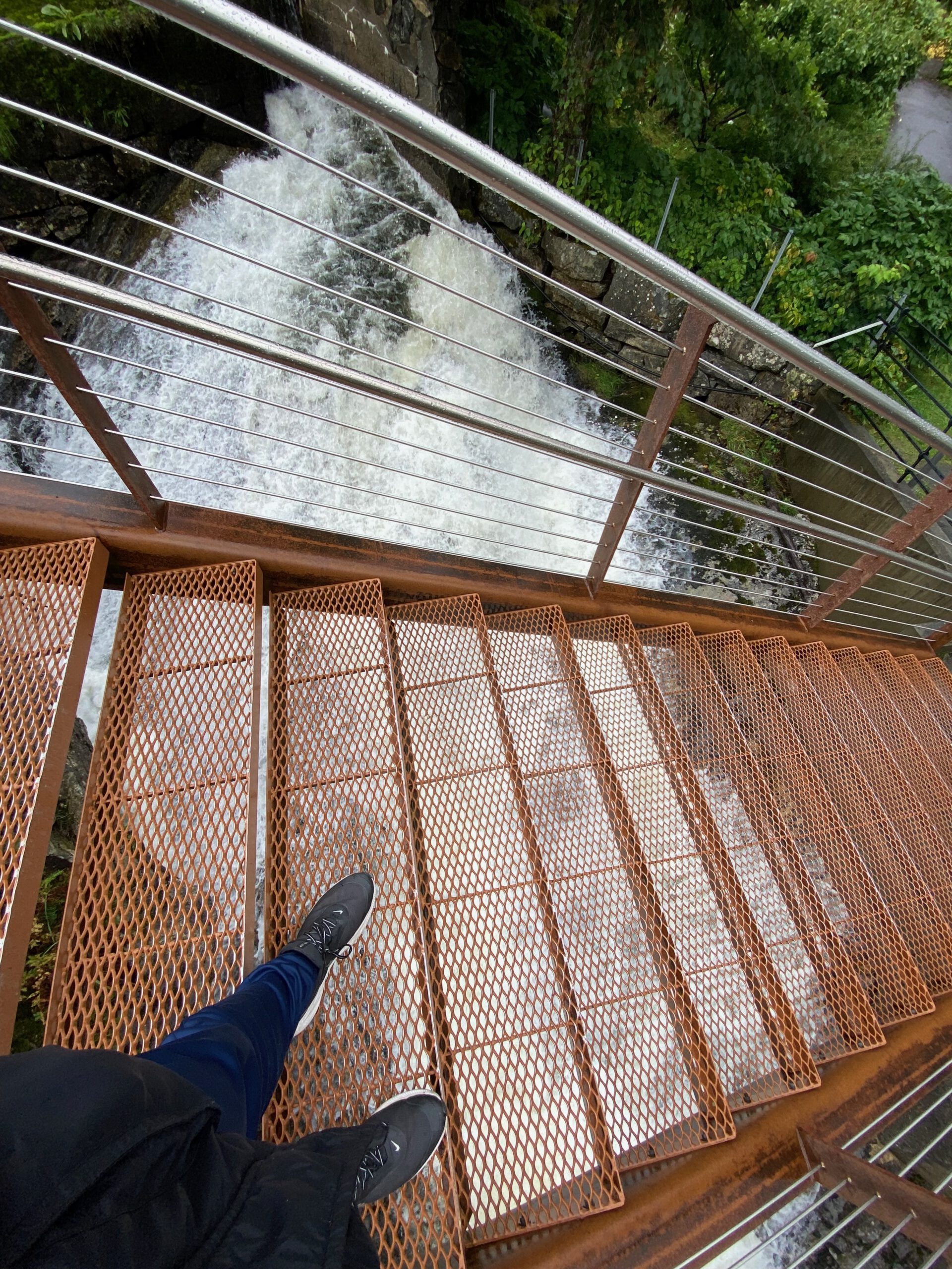 Metal staircase above rushing river at Norsk Fjordsenter Geiranger with view down to waterfall, located in the UNESCO World Heritage Geirangerfjord region