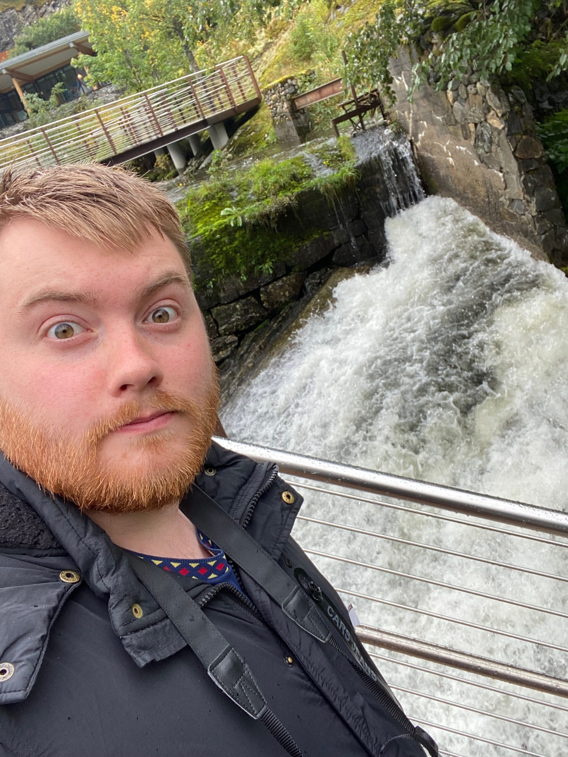 Timo van den Berg aka Timeuw standing near the waterfall at Norsk Fjordsenter Geiranger, part of the UNESCO World Heritage Geirangerfjord experience in Norway