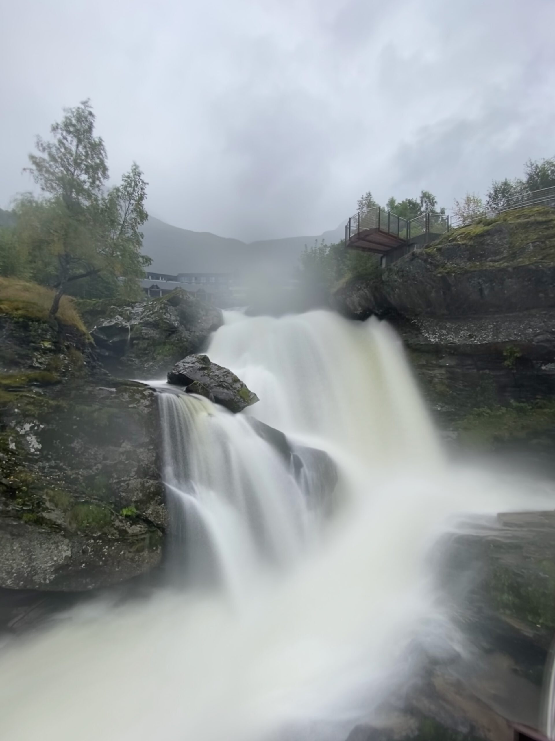 Powerful waterfall near Norsk Fjordsenter Geiranger cascading over rocky cliffs with mist rising above the UNESCO World Heritage Geirangerfjord landscape