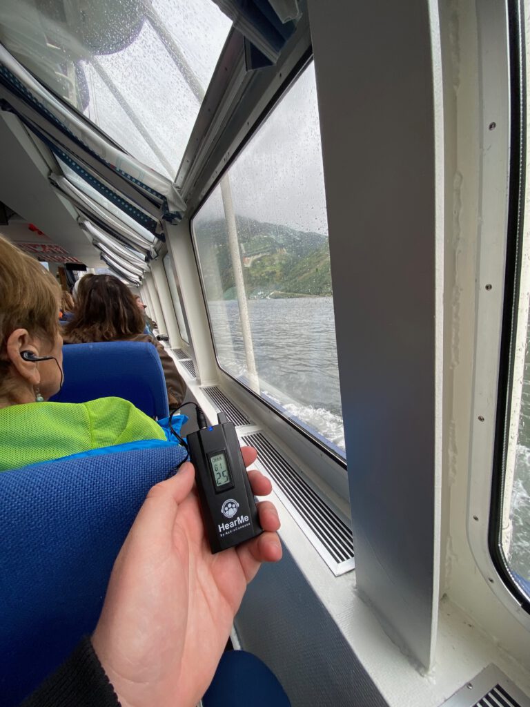 Audio guide device and earphones used during the Geiranger Fjord and Waterfalls Sightseeing Boat Trip inside the boat cabin with fjord view through rain covered windows