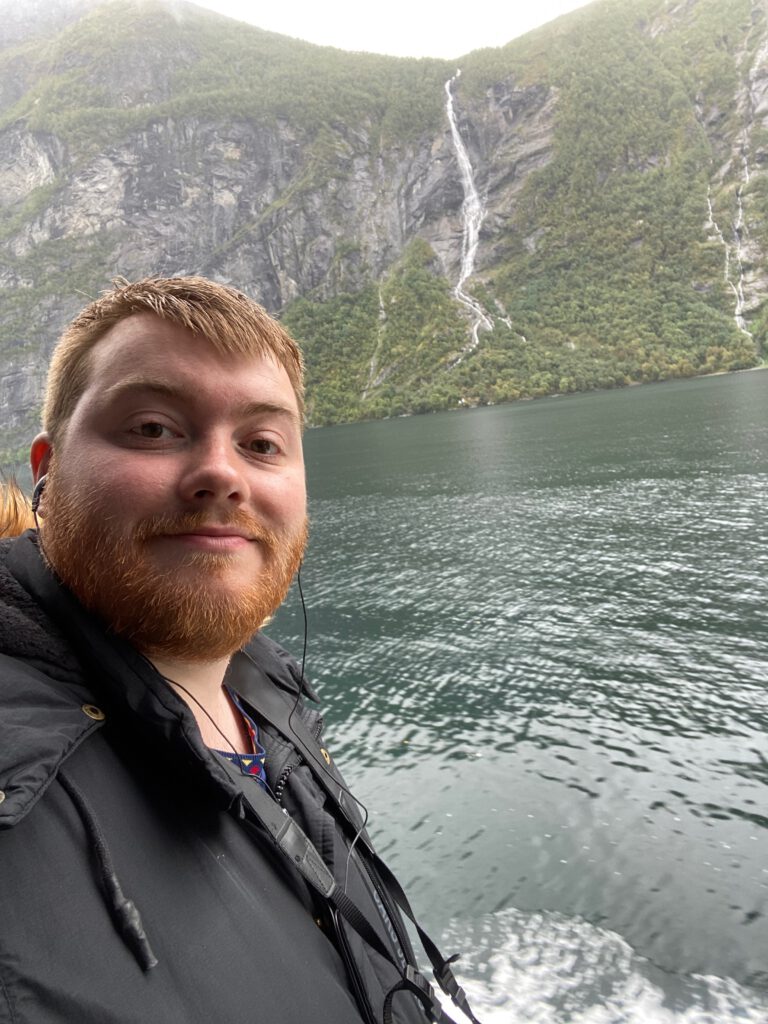 Timo van den Berg Timeuw taking a selfie during the Geiranger Fjord and Waterfalls Sightseeing Boat Trip with waterfall cliffs and fjord scenery in the background