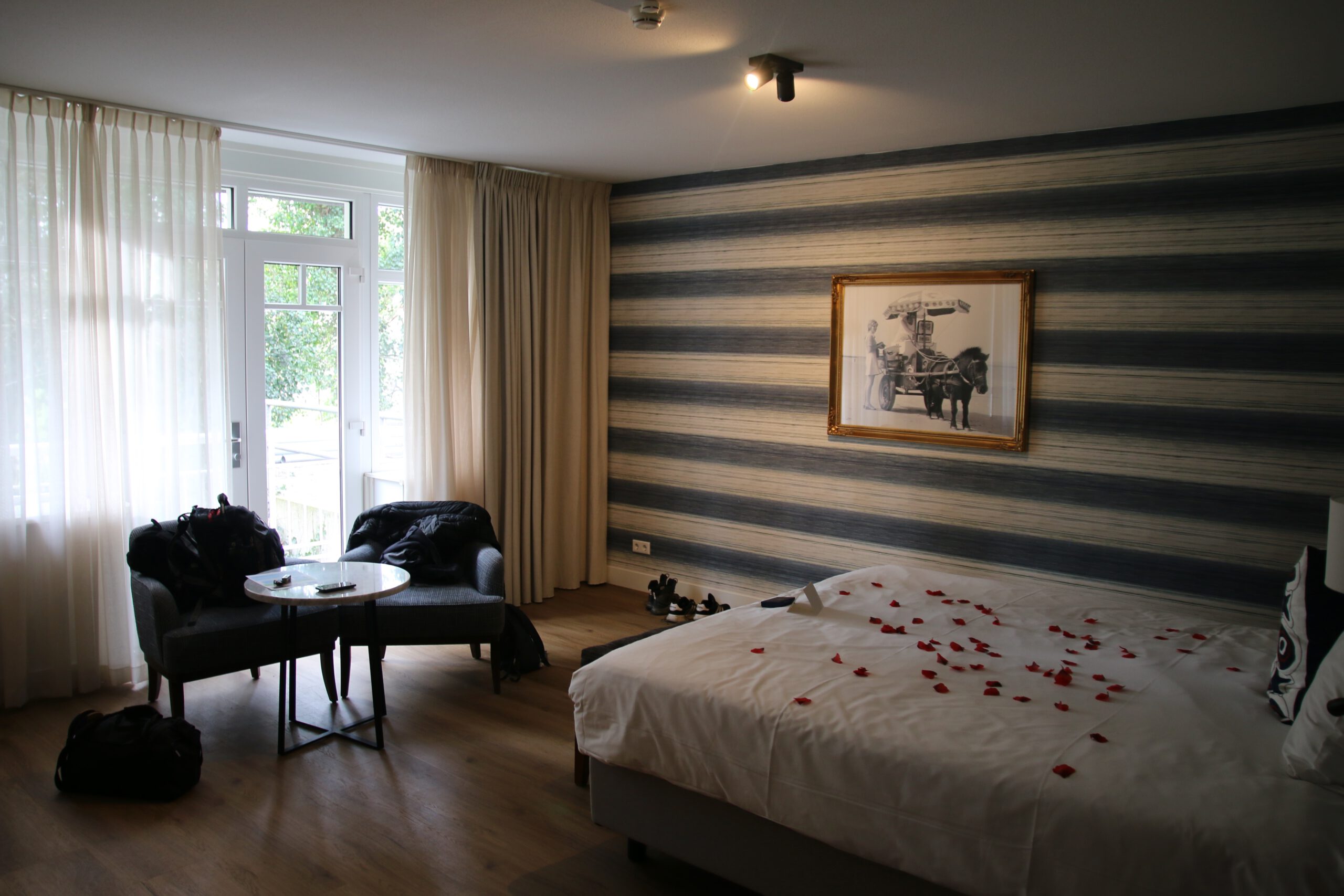 Grand Hotel Ter Duin review room 124 in Burgh Haamstede featuring spacious double bed with rose petals, striped Zeeland accent wall, seating area with armchairs, balcony doors, and modern interior design