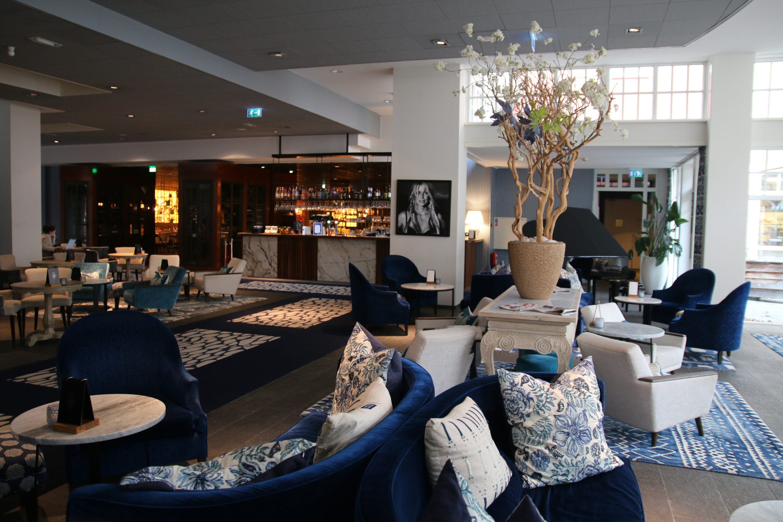 Grand Hotel Ter Duin review lobby interior in Burgh Haamstede showing stylish blue lounge chairs, bar area, grand piano, and modern hotel atmosphere