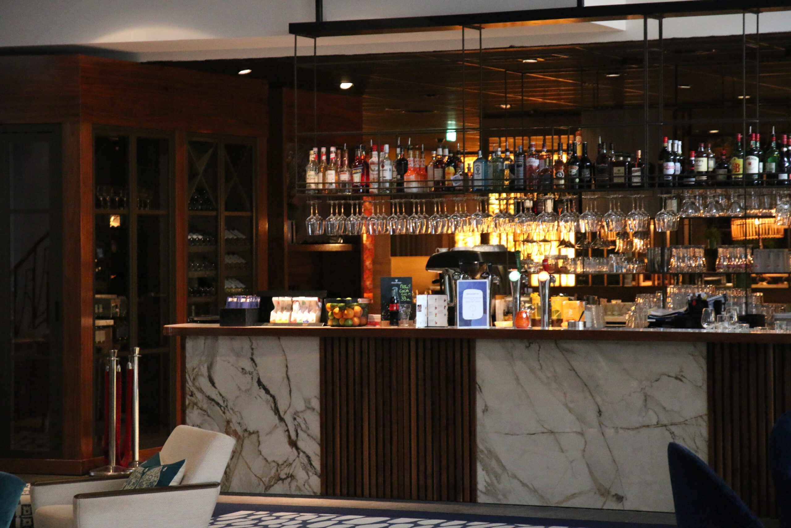 Grand Hotel Ter Duin review hotel bar area in Burgh Haamstede featuring marble counter, hanging wine glasses, premium liquor selection, and warm lounge atmosphere