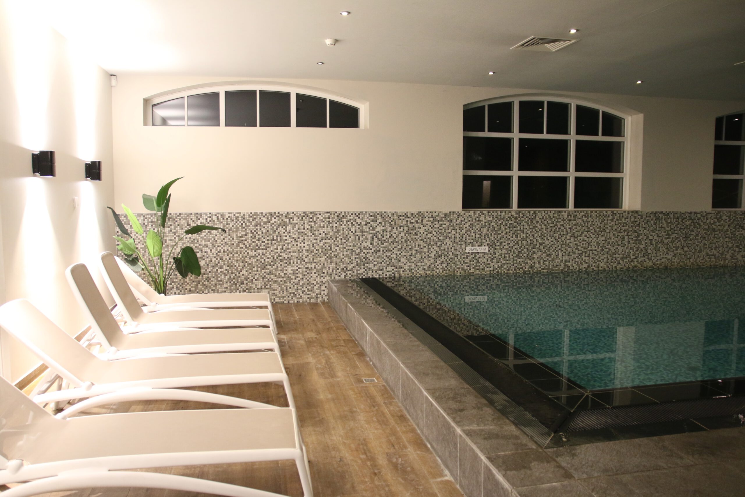 Grand Hotel Ter Duin spa review – white lounge chairs next to the indoor pool with mosaic tile walls and soft lighting inside the hotel wellness area.