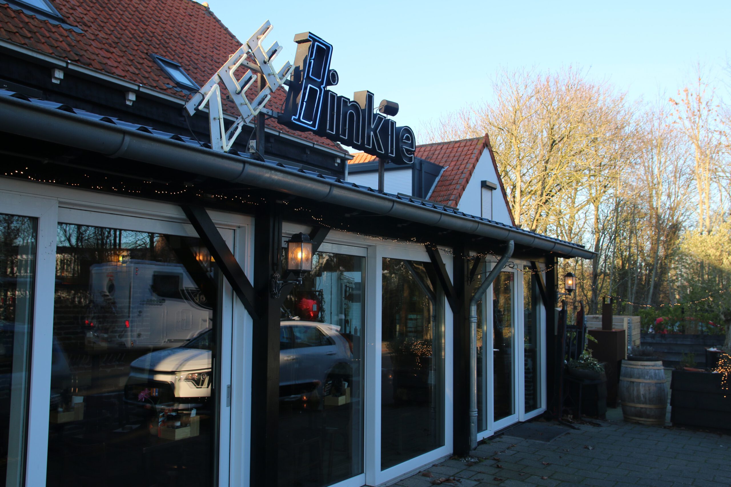 Restaurant Zeebinkie review, exterior view of Restaurant Zeebinkie in Burgh Haamstede with illuminated Binkie sign, red tiled roof, glass windows, cozy lantern lighting and evening blue sky in Zeeland